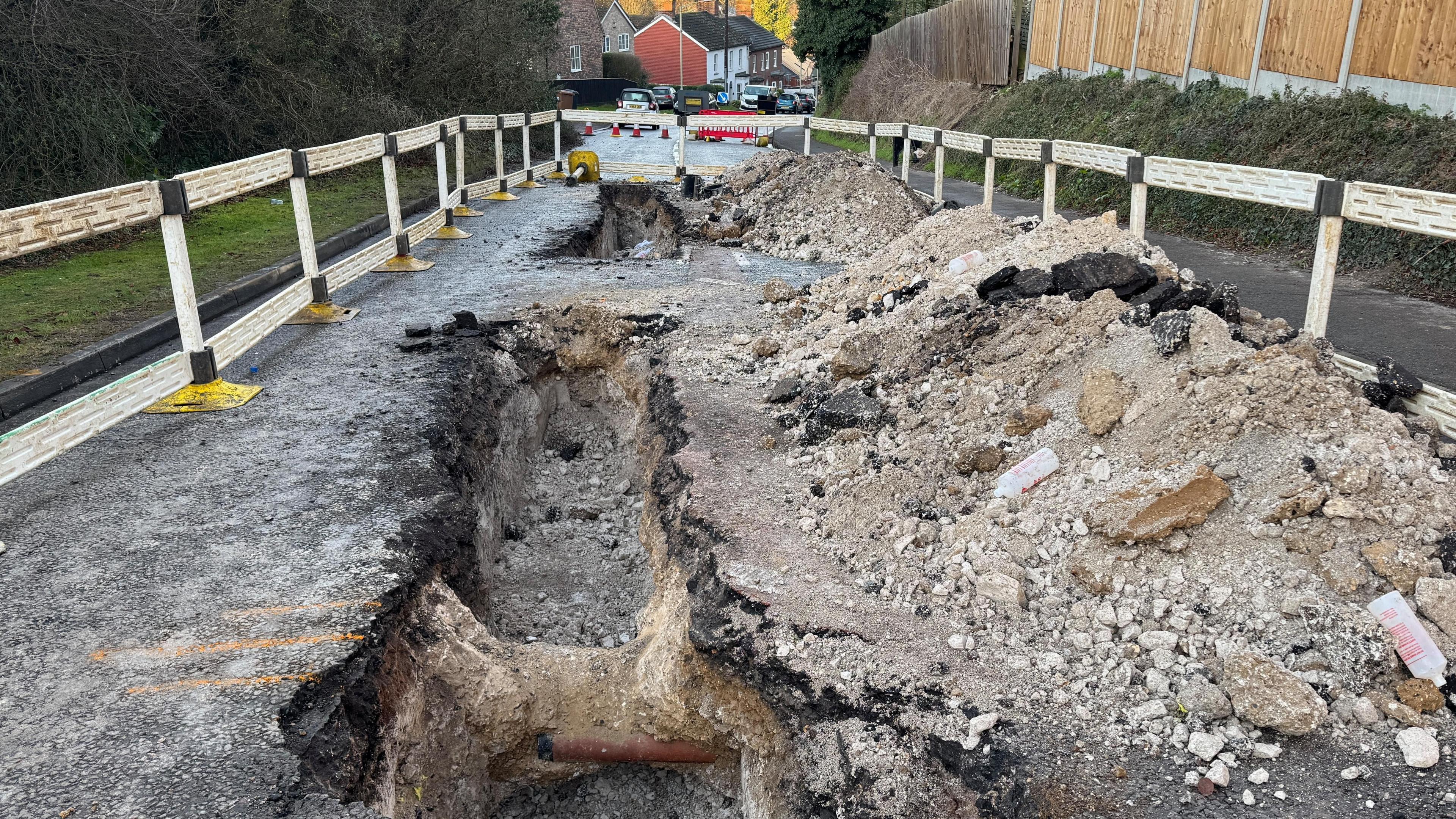 A road that has been dug up by engineers to fix a gas leak revealing a large hole, which has been cordoned off.