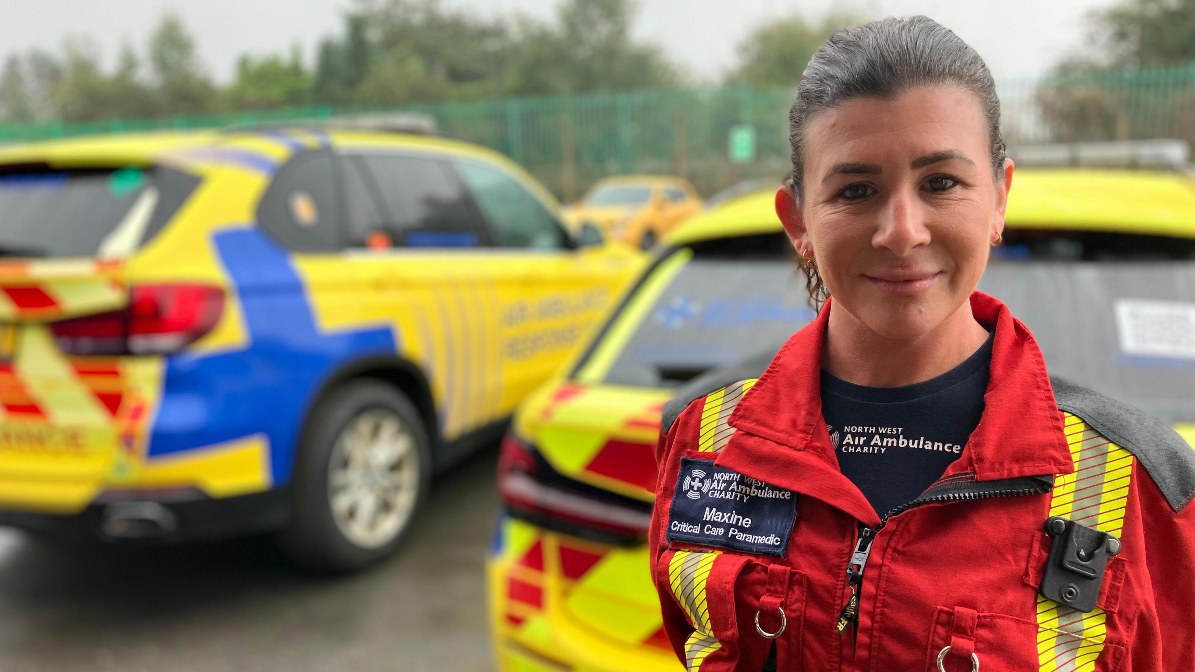 Maxine Sharples wearing a red and yellow uniform in front of emergency vehicles