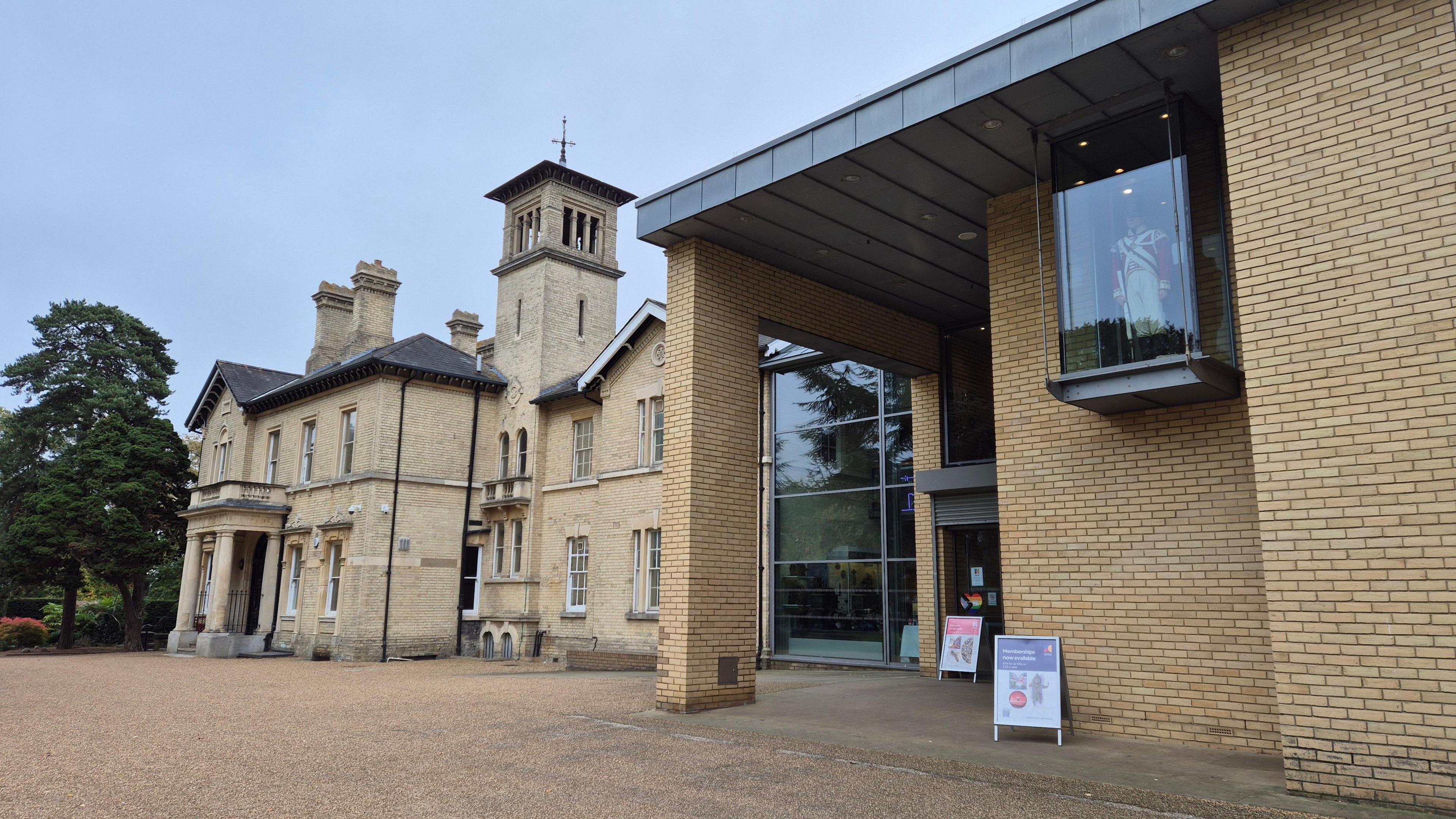 A wide shot of the front of a museum with sand coloured bricks and a soldier encased in glass high up on the outside of the building.