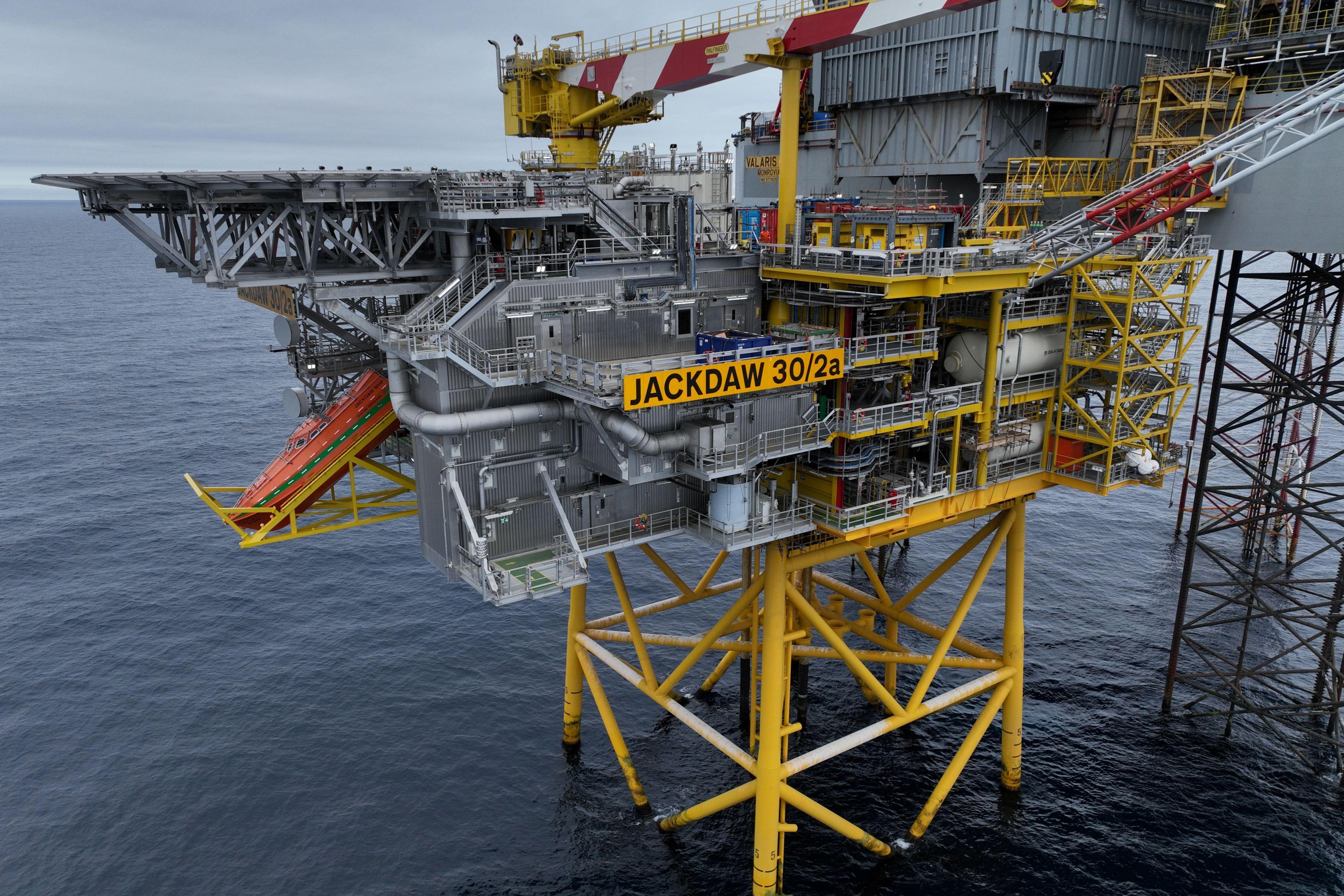 Offshore oil and gas platform marked “JACKDAW 30/2a” standing on yellow support legs above the sea, with industrial equipment, pipework and a crane visible under a partly cloudy sky.
