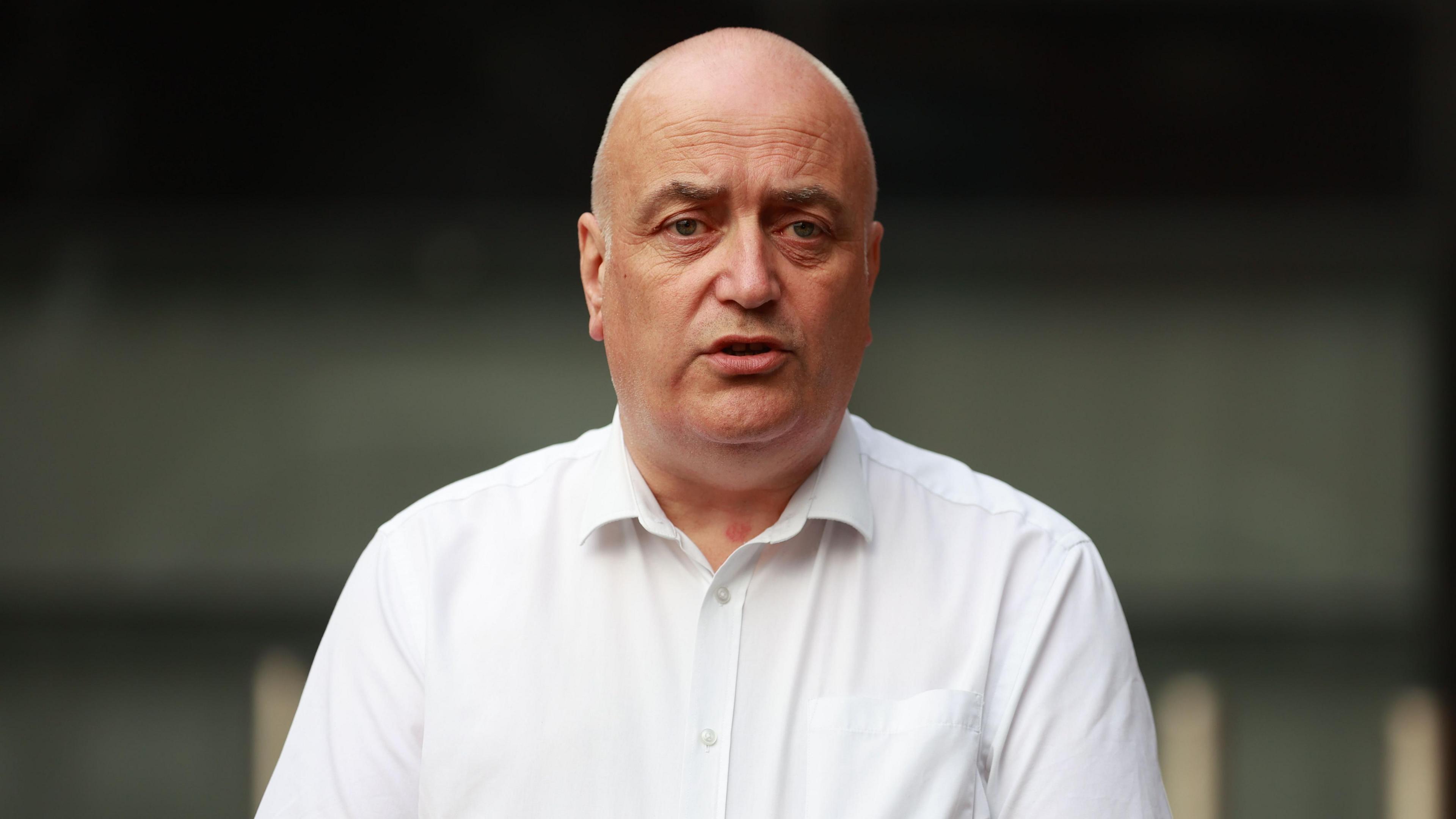 Trevor Clarke, a bald man, wearing a white shirt. The background of the image is blurred.