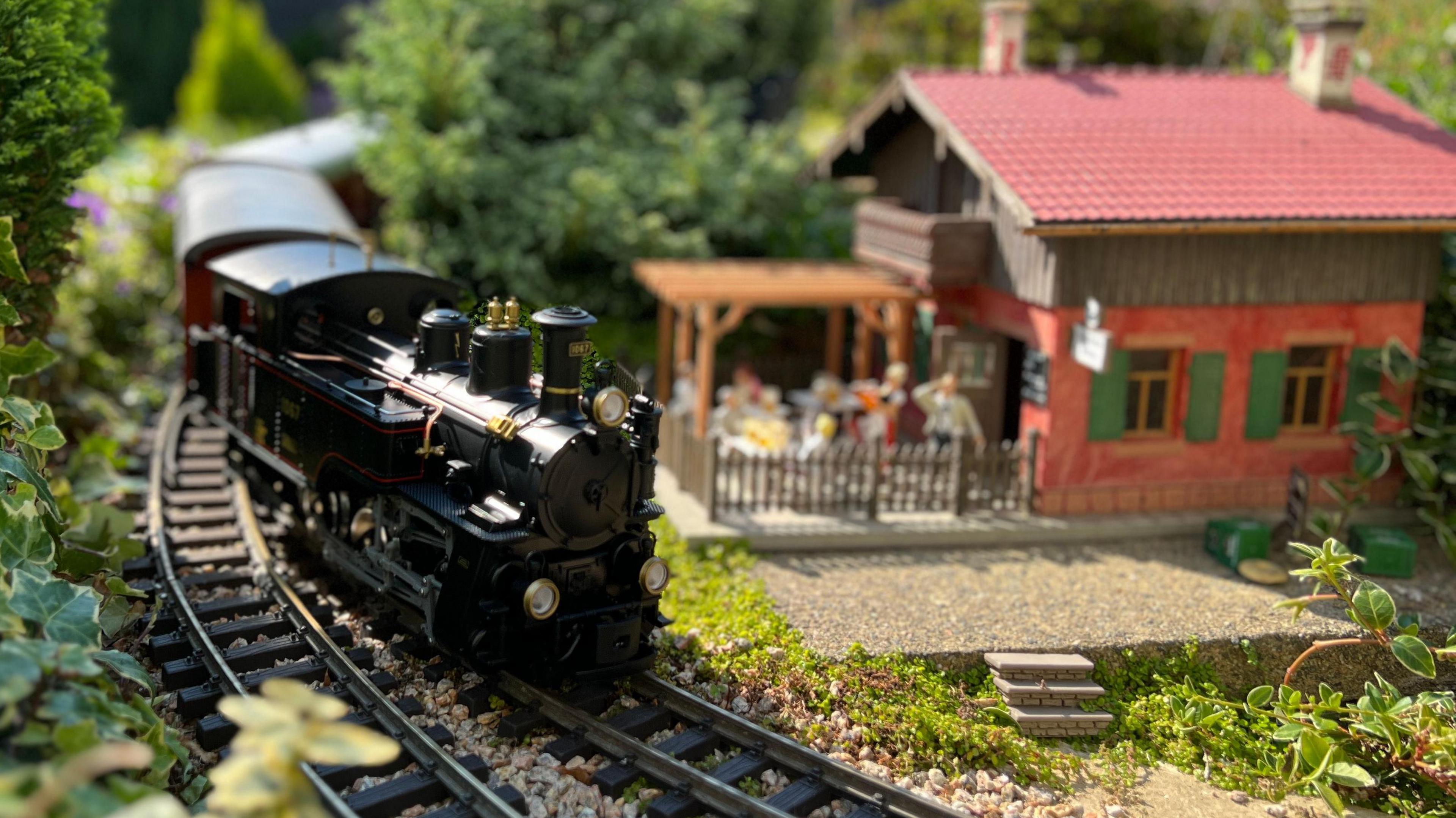 A black model train is passing a replica beer garden