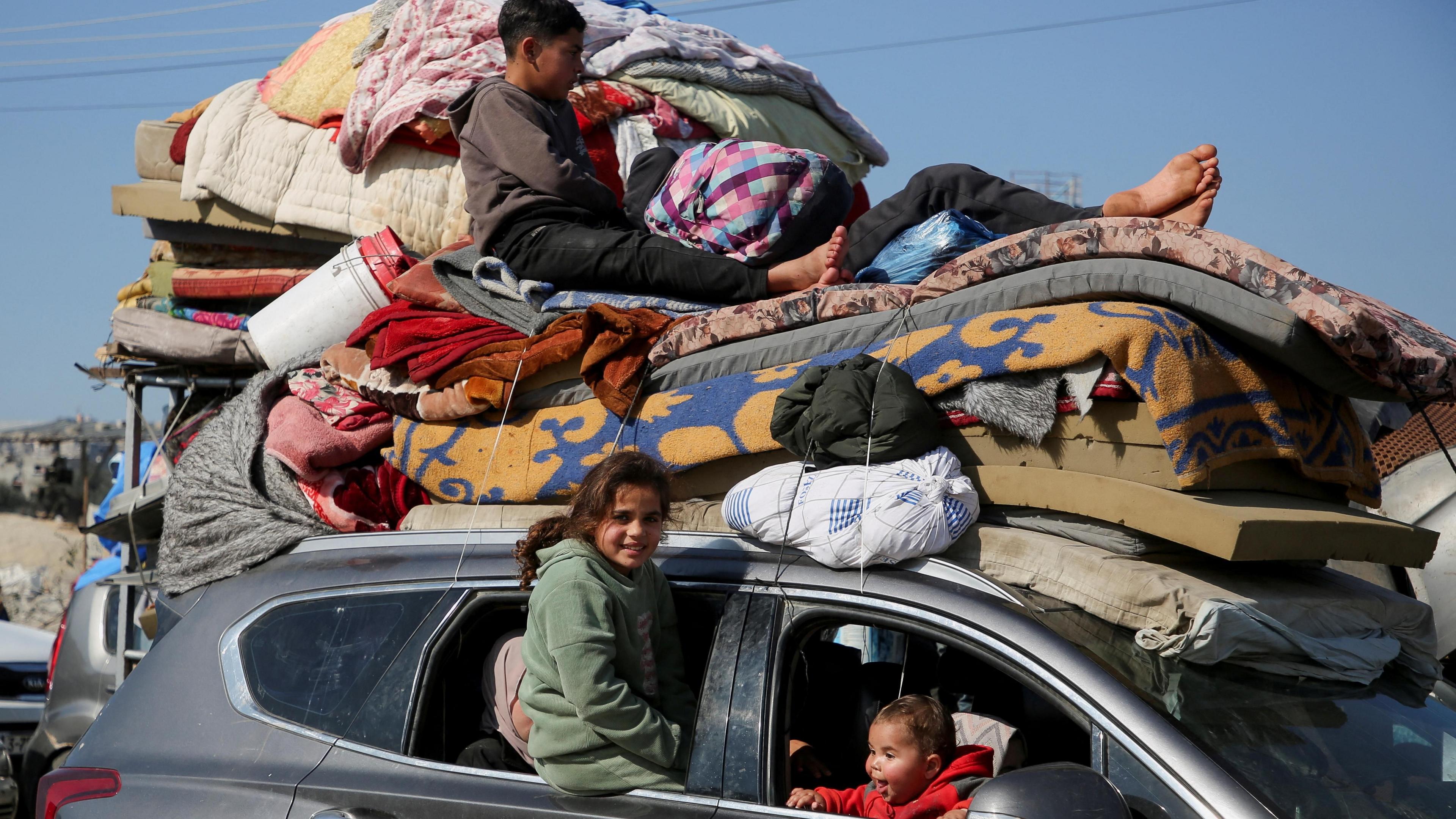 Palestinian children sit inside and on top of a car piled high with blankets, mattresses and other possessions which is queuing to go through a screening area on Salah al-Din Street, in the Netzarim corridor, in central Gaza (27 January 2025)