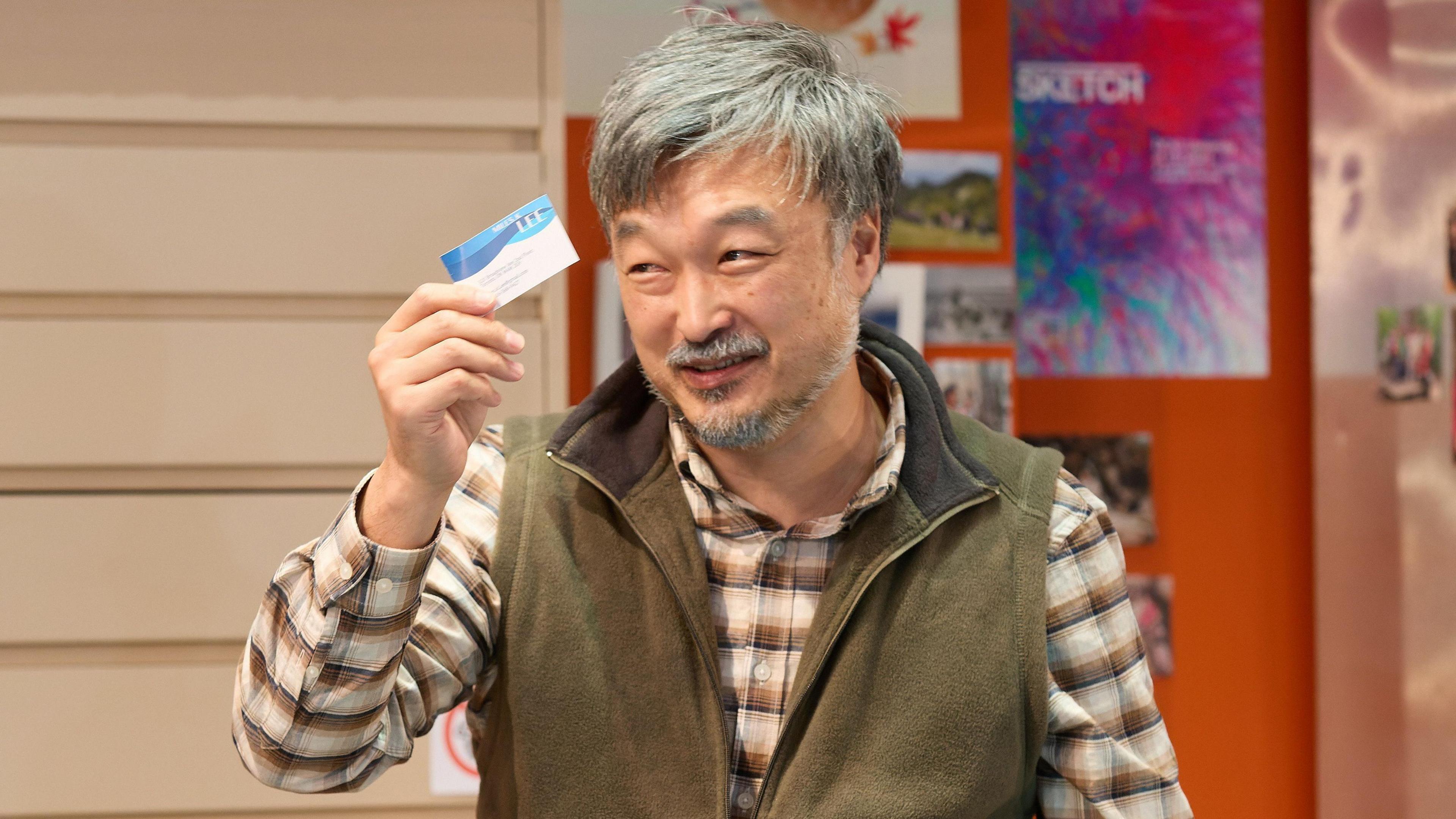 Ins Choi performing in Kim's Convenience, holding up a business card