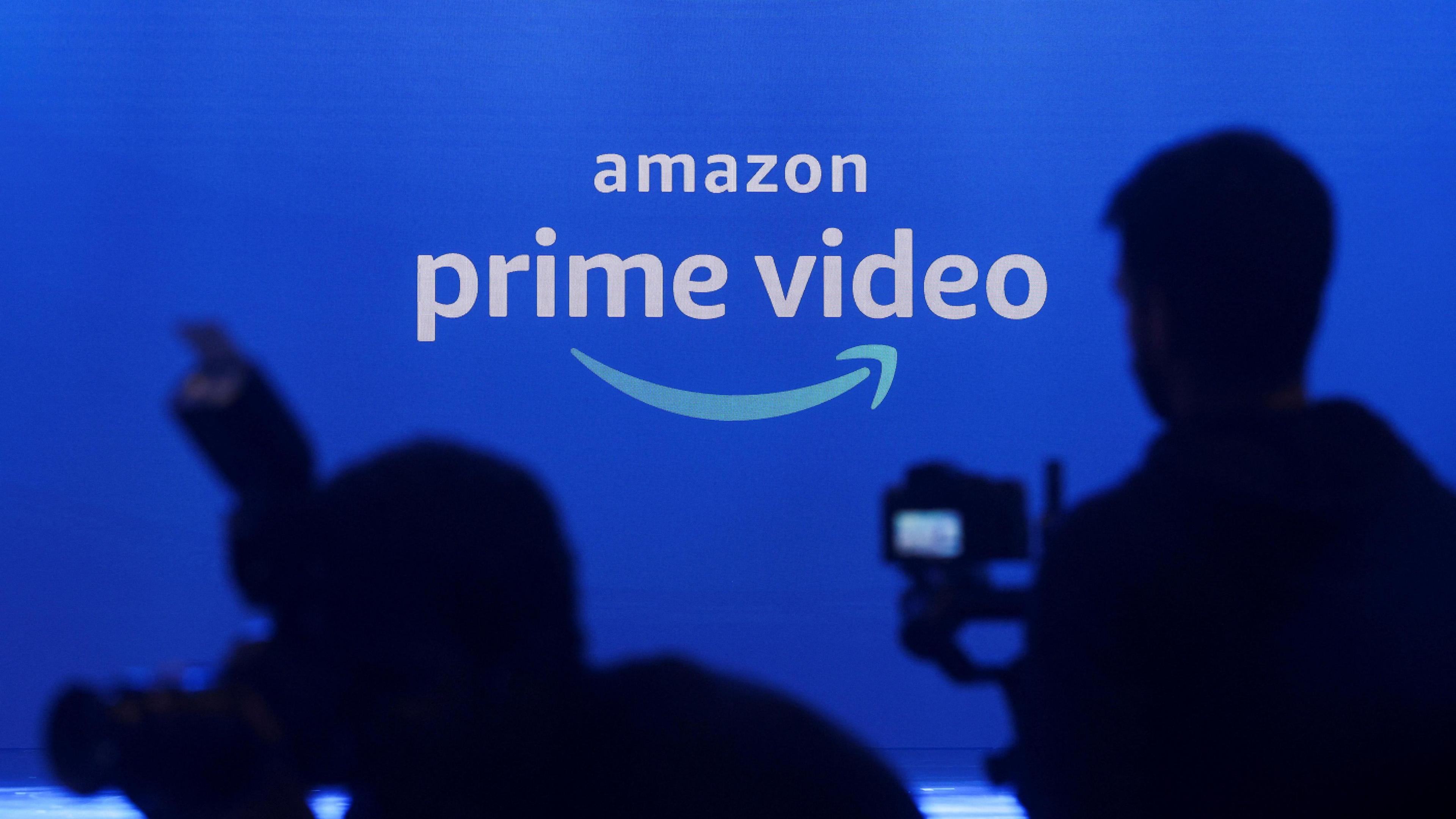 the Amazon Prime Video logo projected on a screen as photographers in shadow aim their cameras.