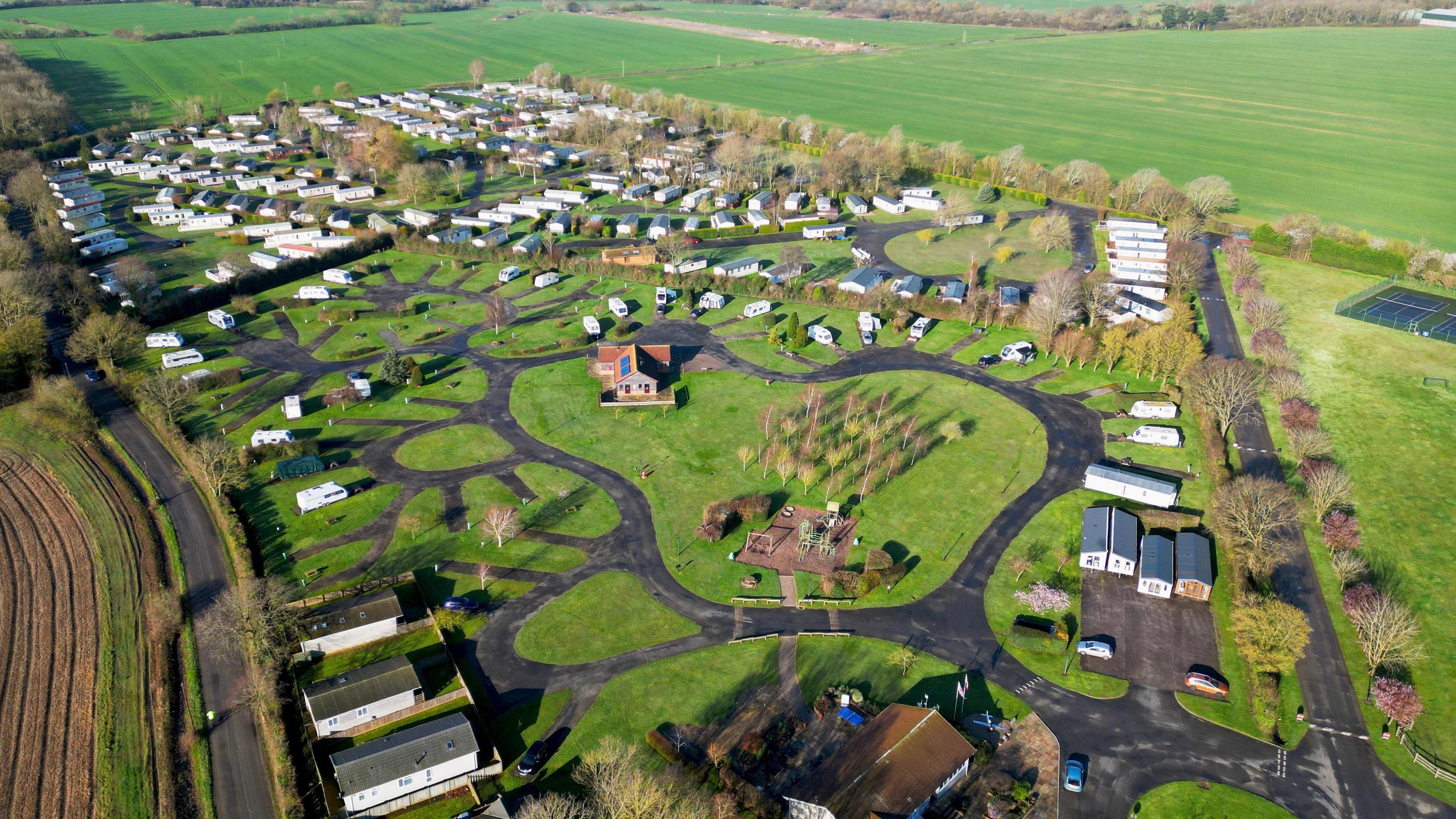 An aerial shot of the Cakes and Ale Holiday Park. It is show a large plot of land with caravans and buildings on it. 