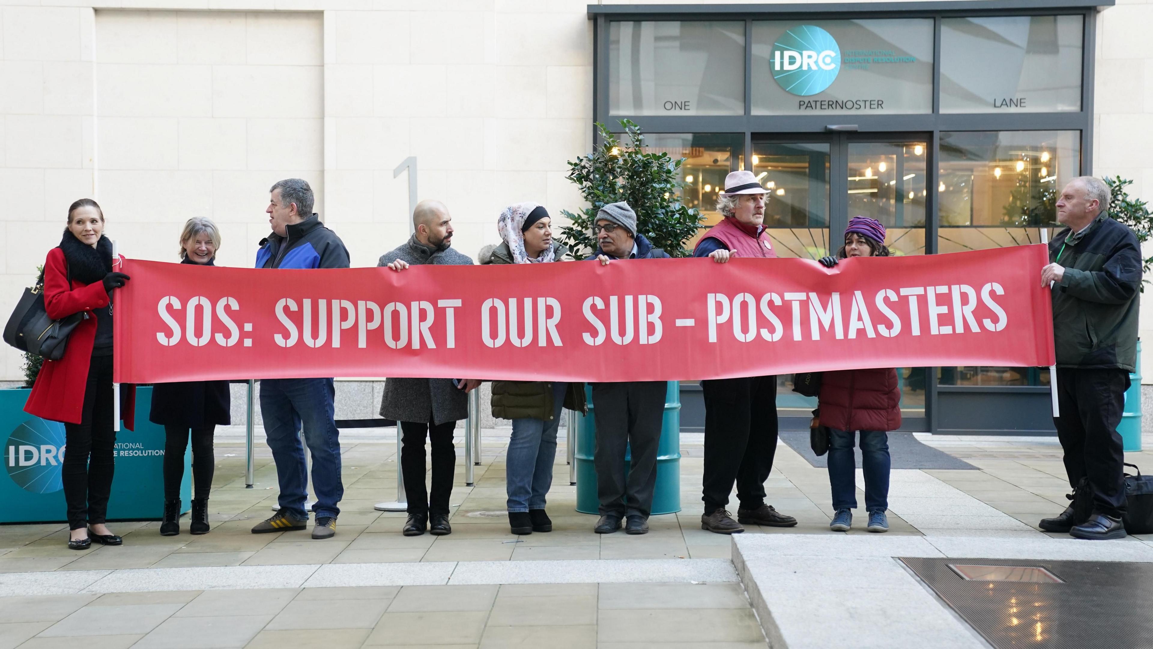 Demonstrators protest outside the Post Office Horizon IT inquiry, holding a banner which reads: "SOS: Support our sub-postmasters"