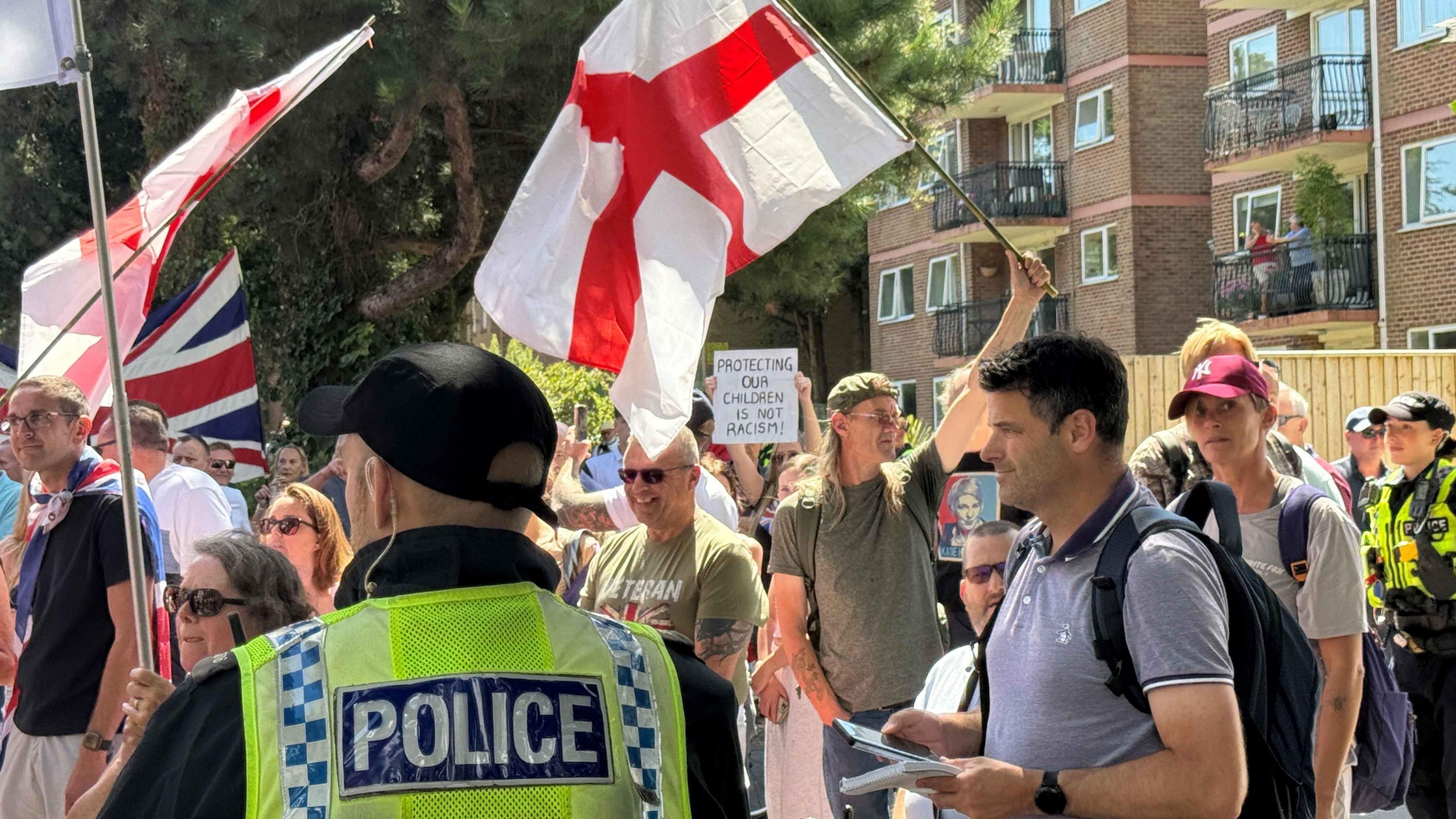 Union Jacks and England flag being waved as anti-immigration protestors gather and riot police are in place.