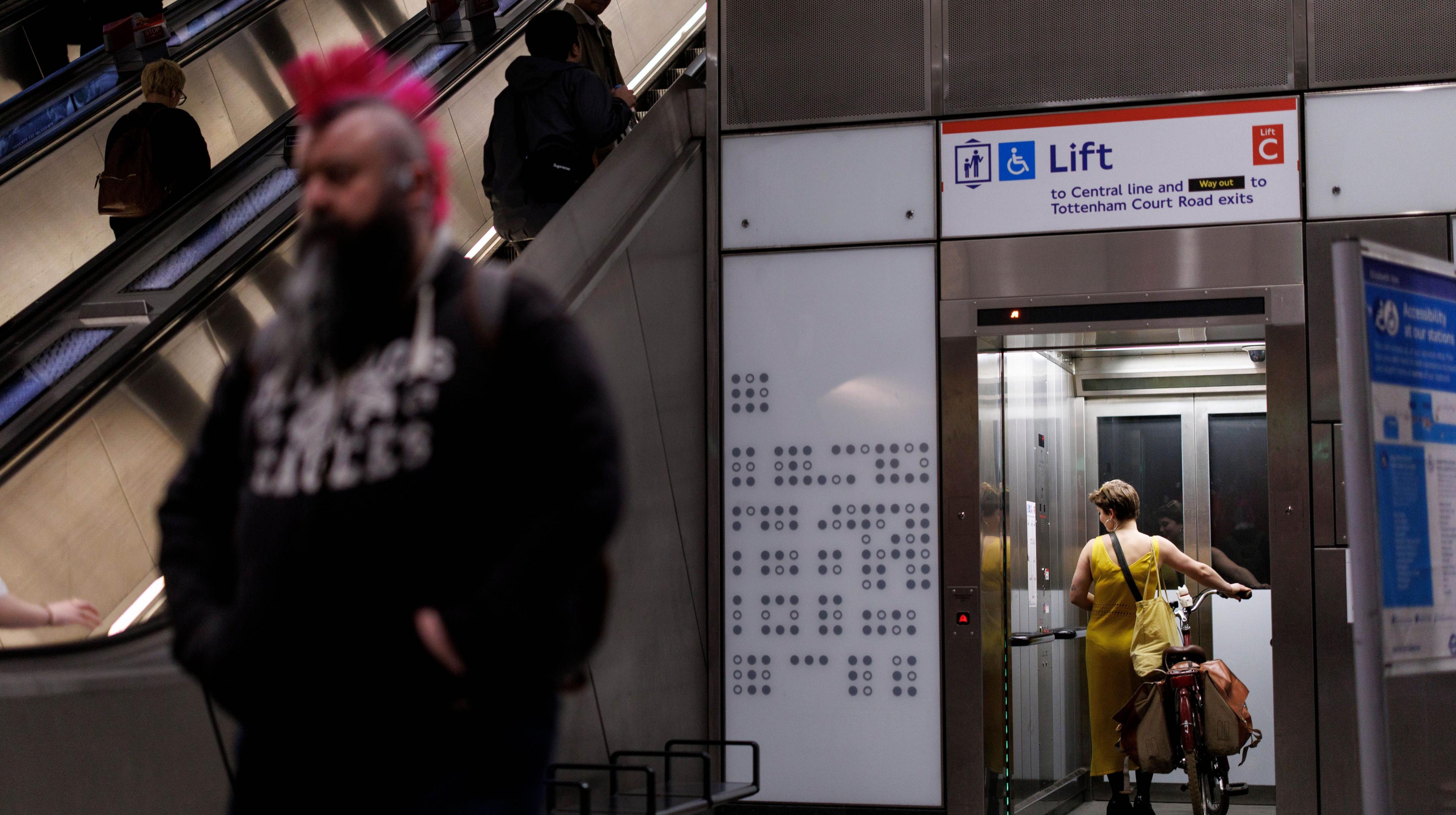 A person waits in a lift at Tottenham Court Road station as people travel down an escalator to the London Underground