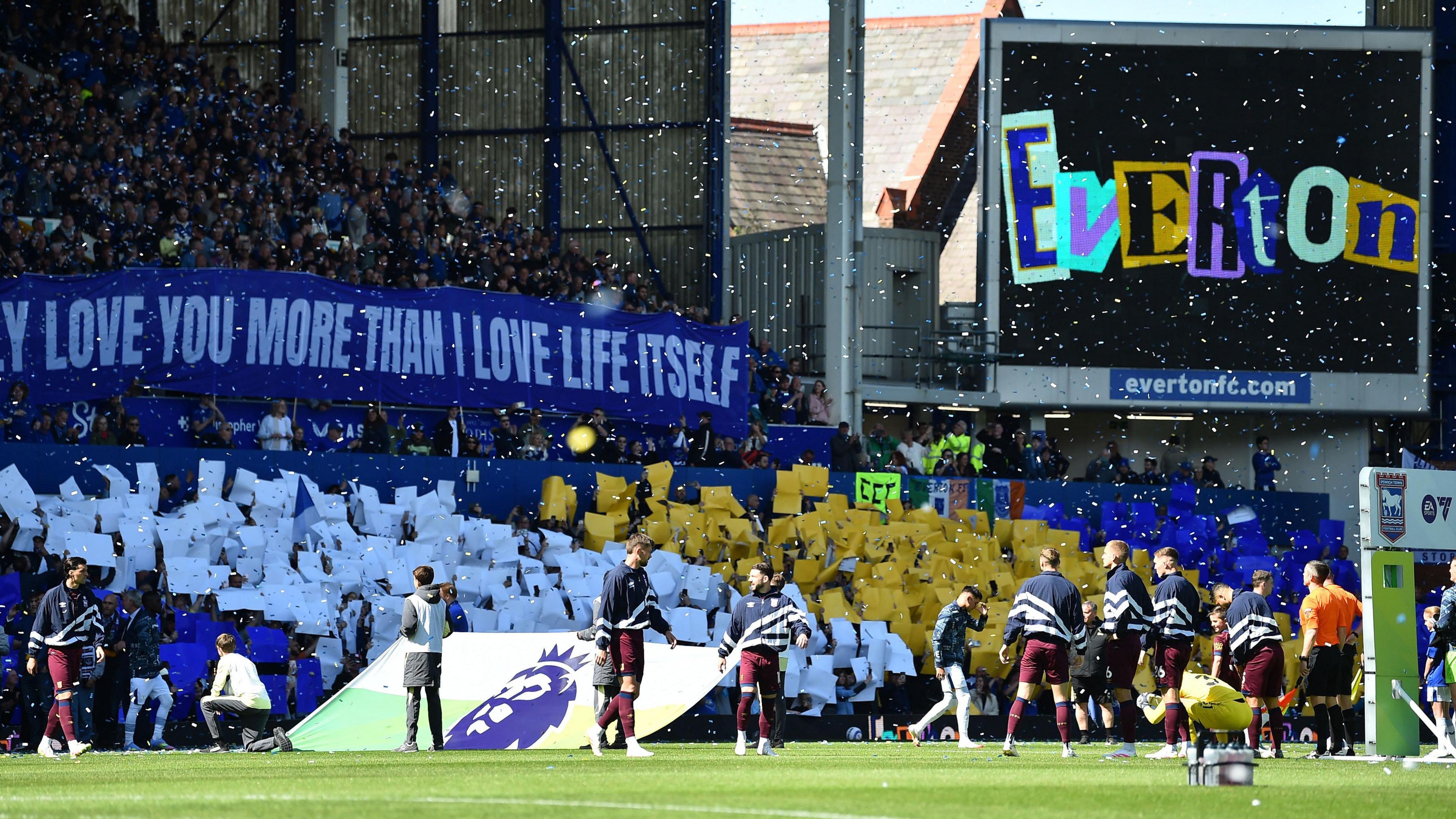 Everton supporters hold up cards and banners as players walk on to the field at Goodison Park