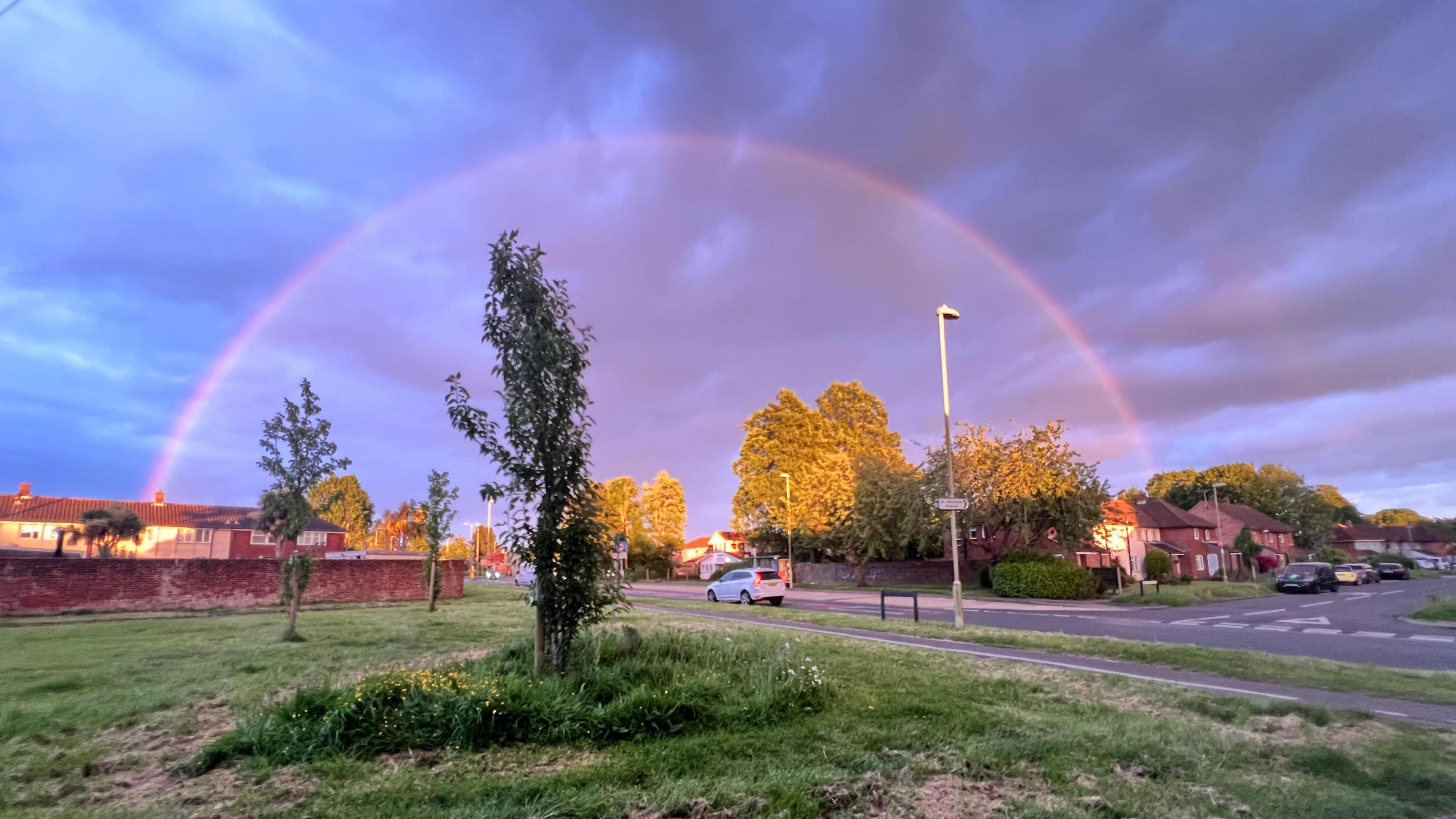 A semi-circular rainbow over the top of a road and houses