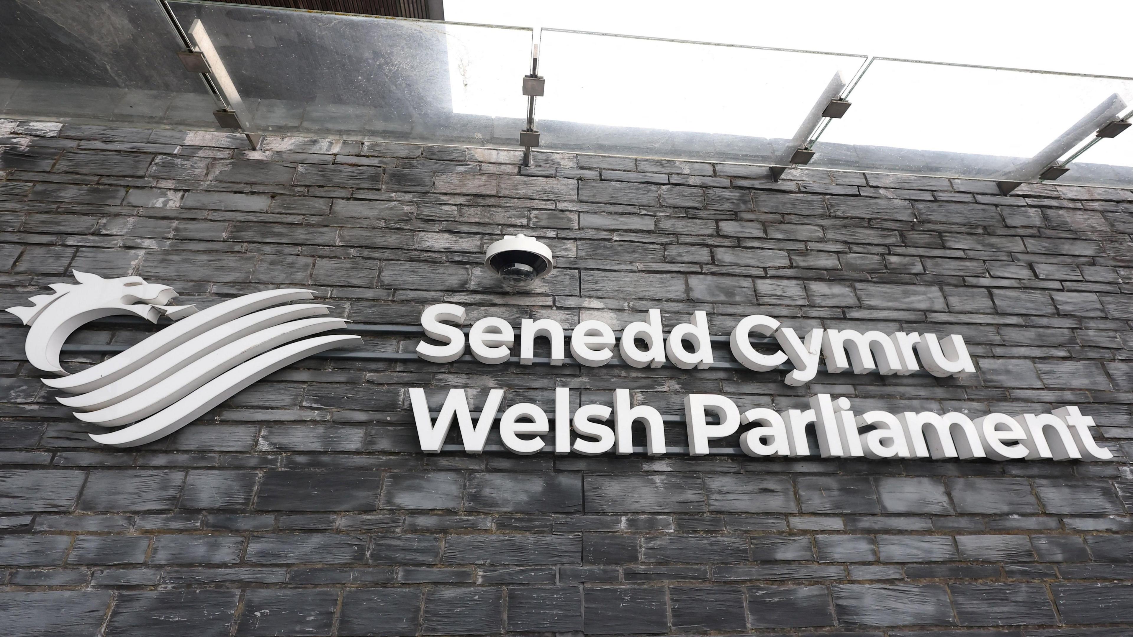 the outside of the Senedd, with a sign that reads Senedd Cymru Welsh Parliament