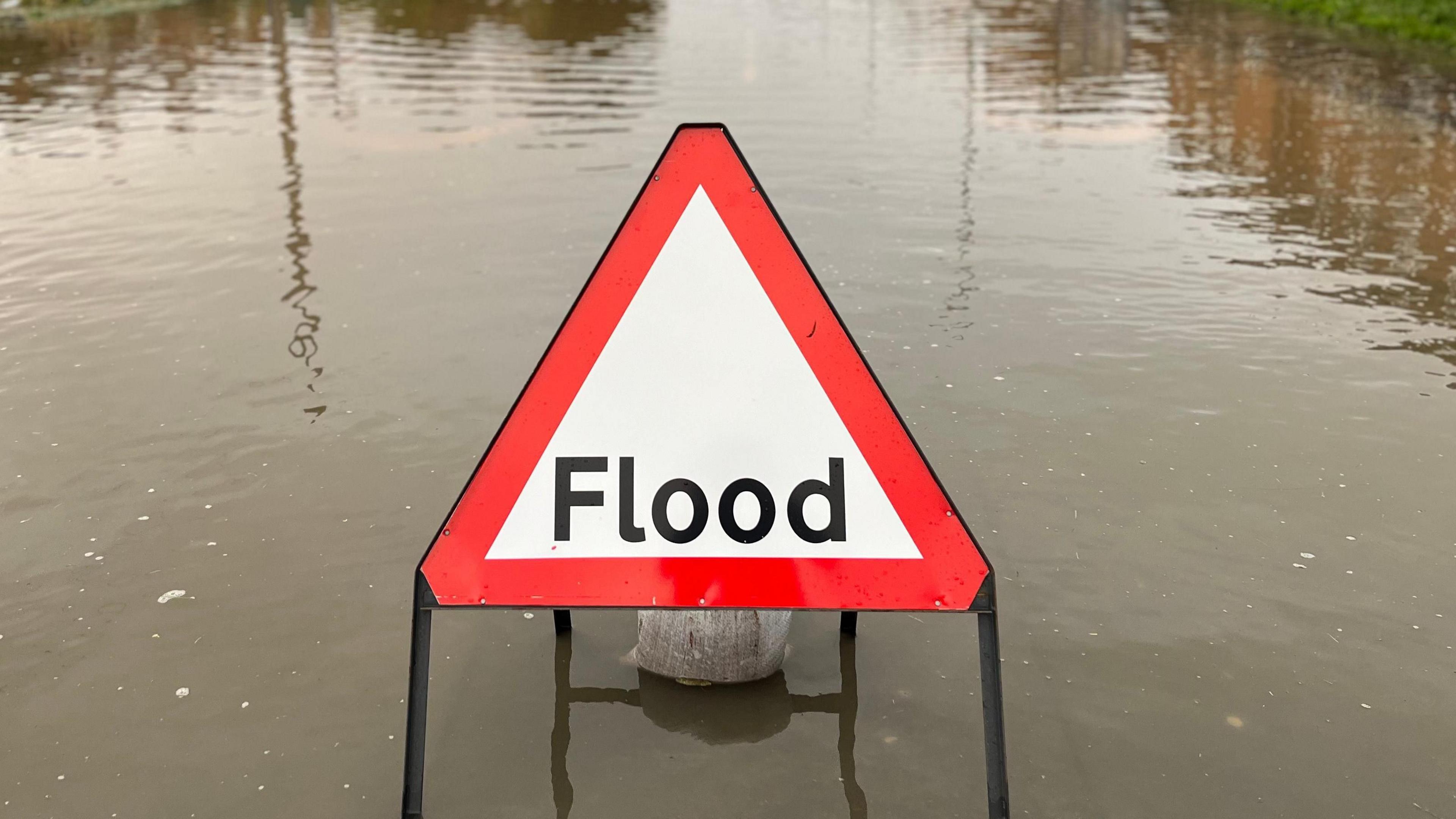 General view of a red flood sign sitting in water on a road.