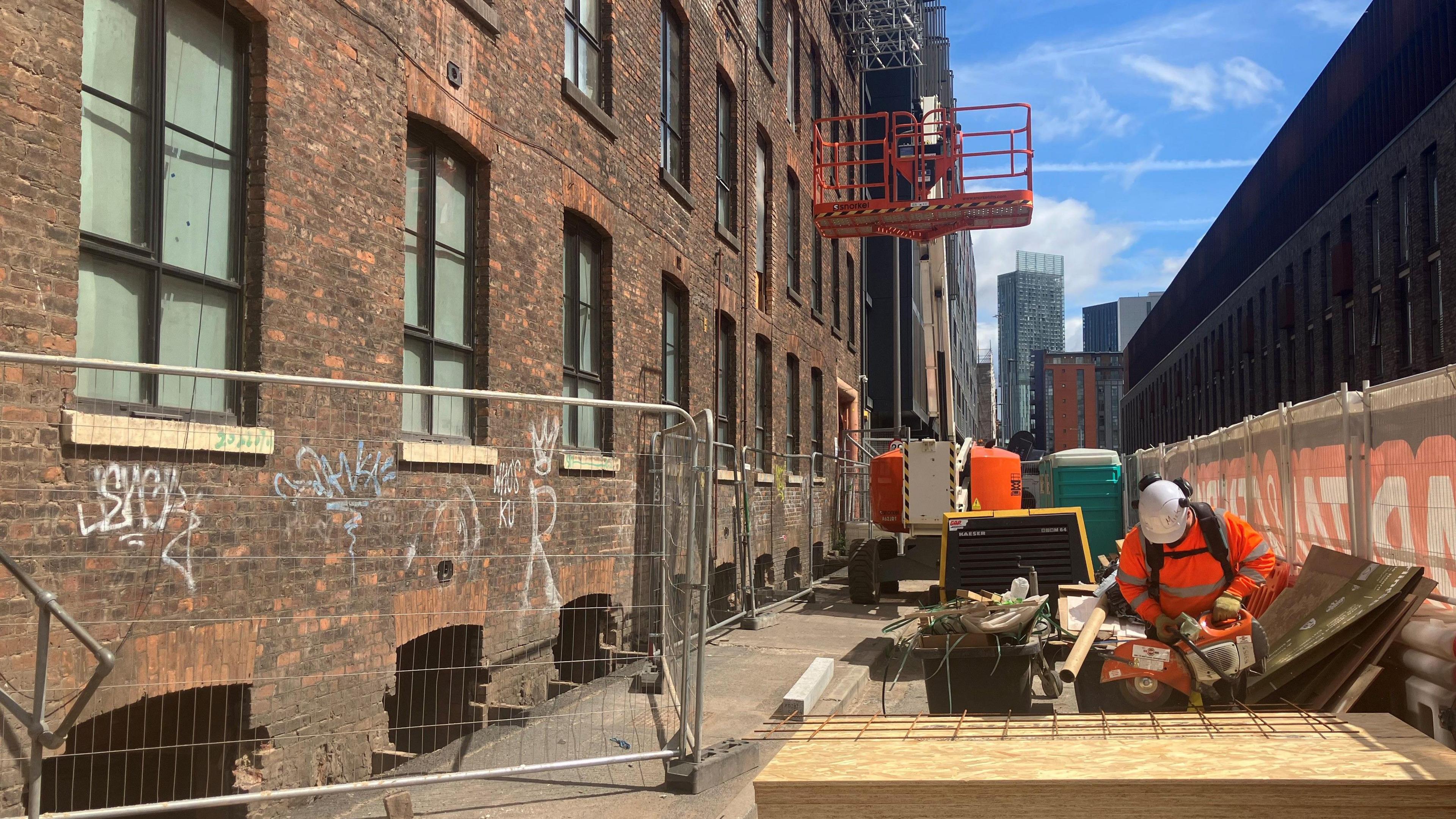 Photograph of Talbot Mill - a Victorian mill in Castlefield. There is a construction worker and building materials in the foreground.