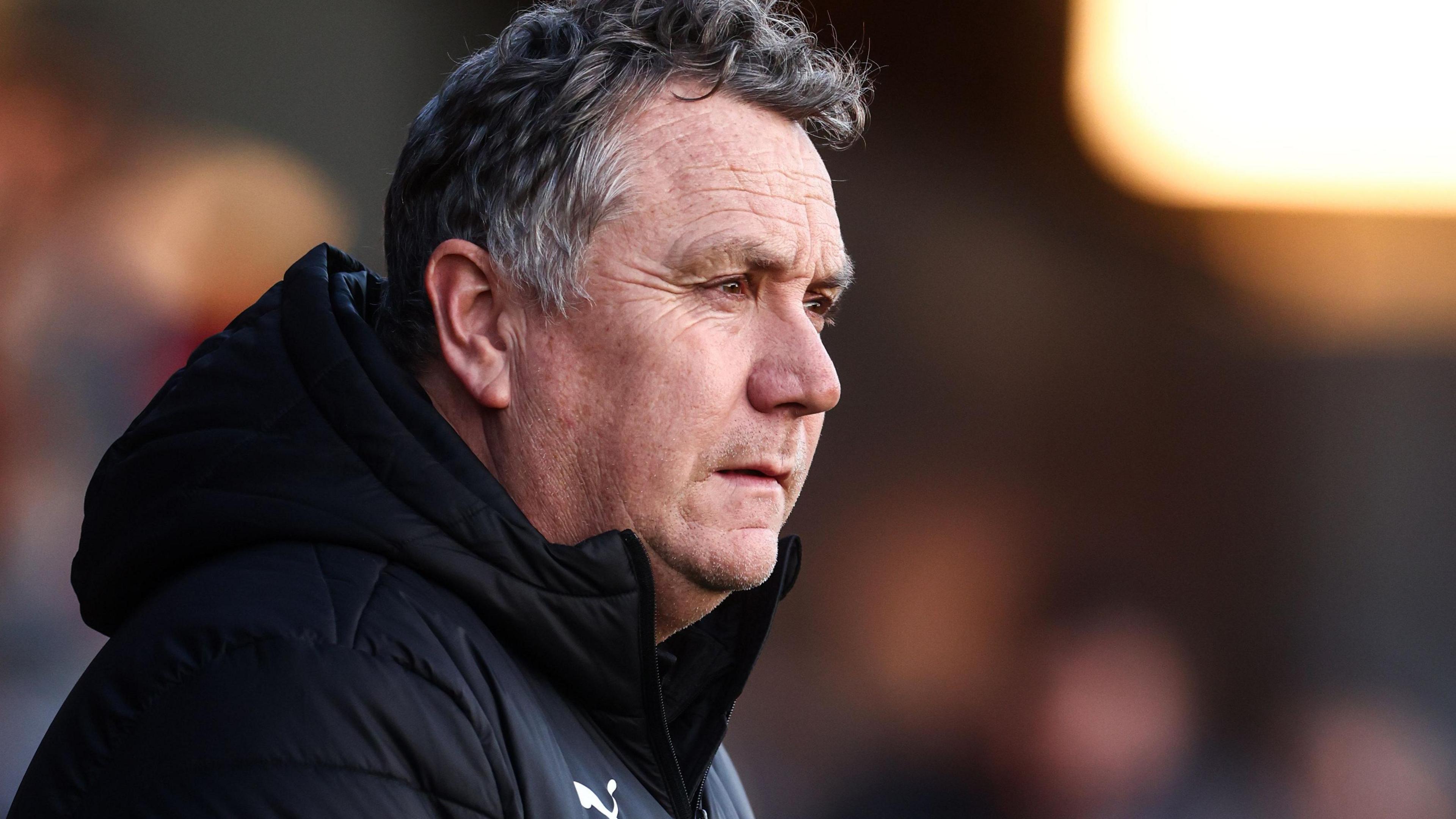 Micky Mellon, wearing a black coat with the hood down, watching Oldham play