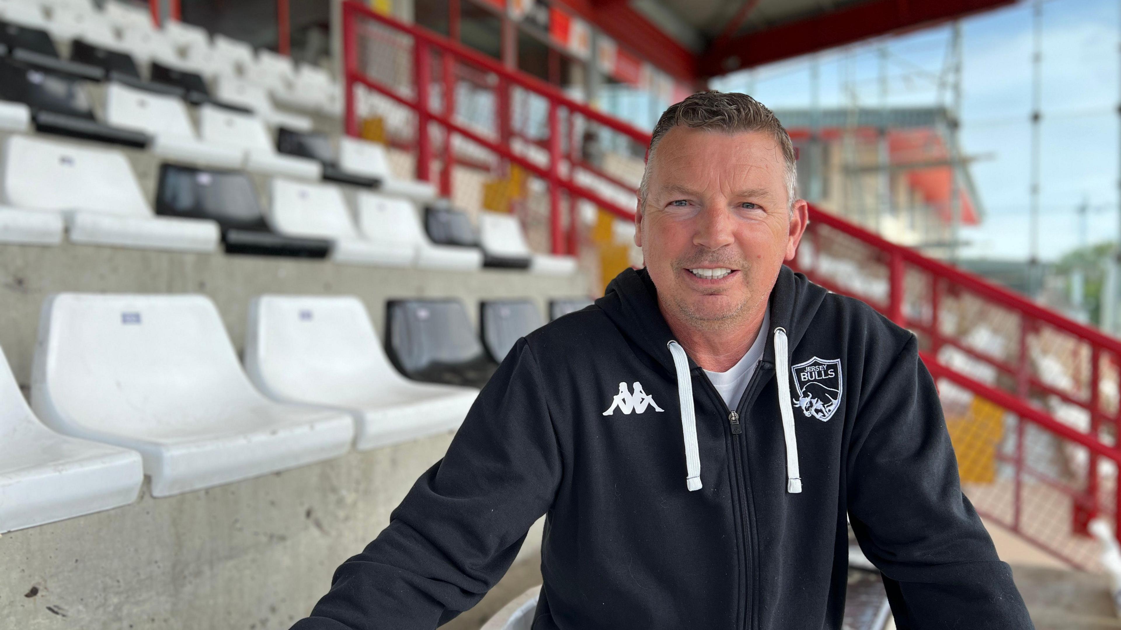 Adie smiles at the camera as he sits in the football stands