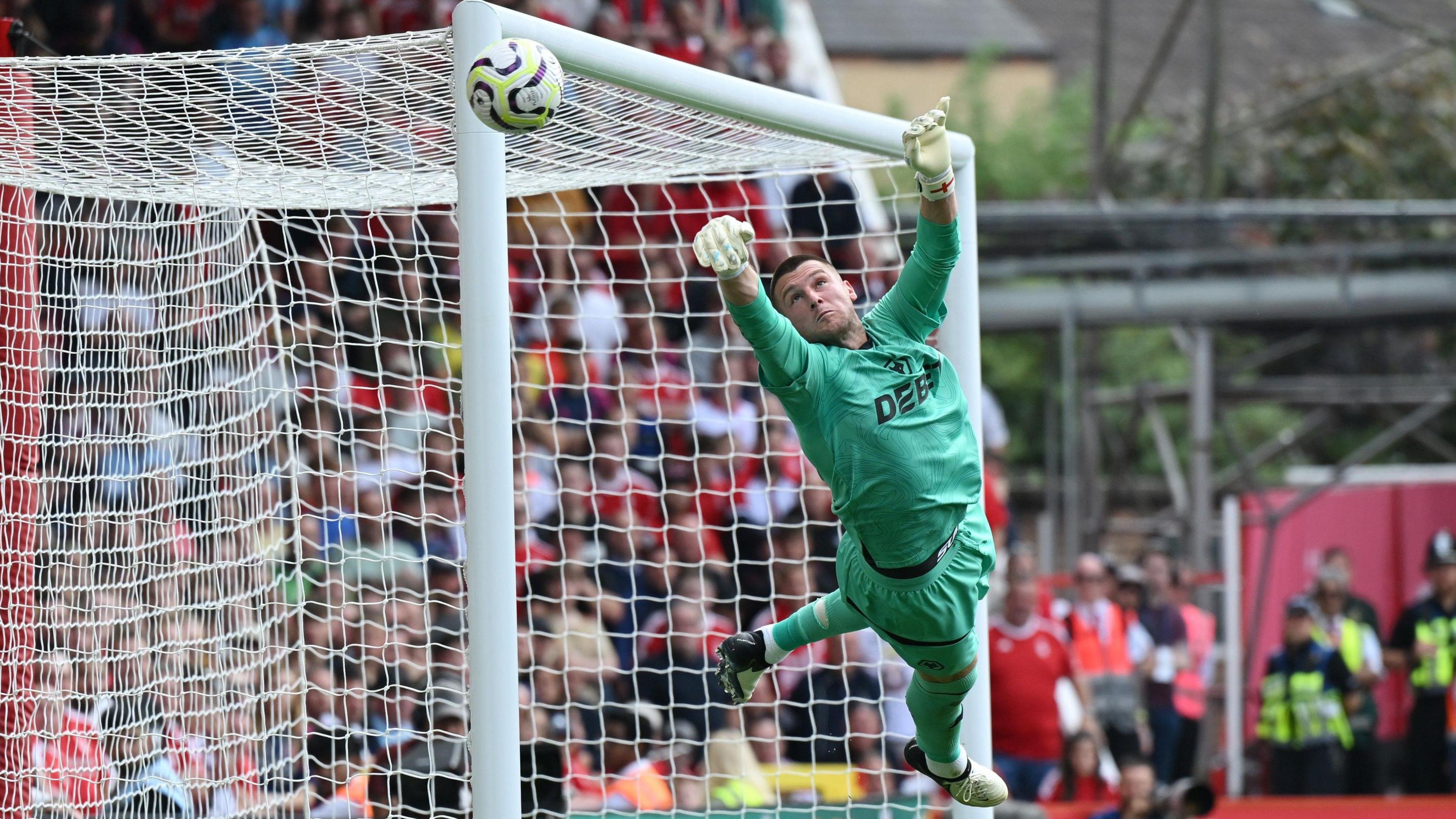 Sam Johnstone, wearing Wolves' green goalkeeping kit, dives up to his right as the ball goes past the post at Nottingham Forest.