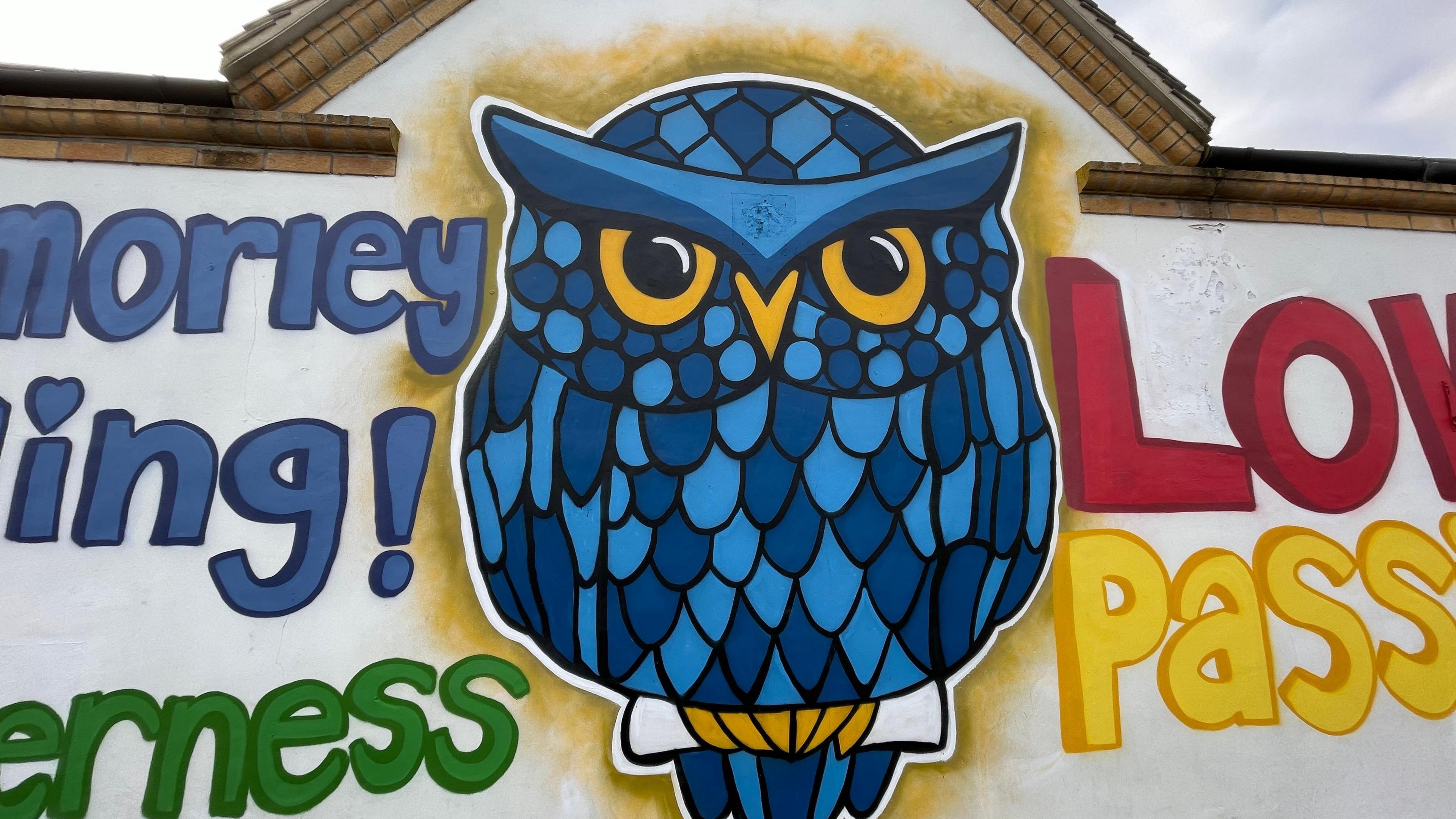 A cartoon owl with blue feathers on a white wall 