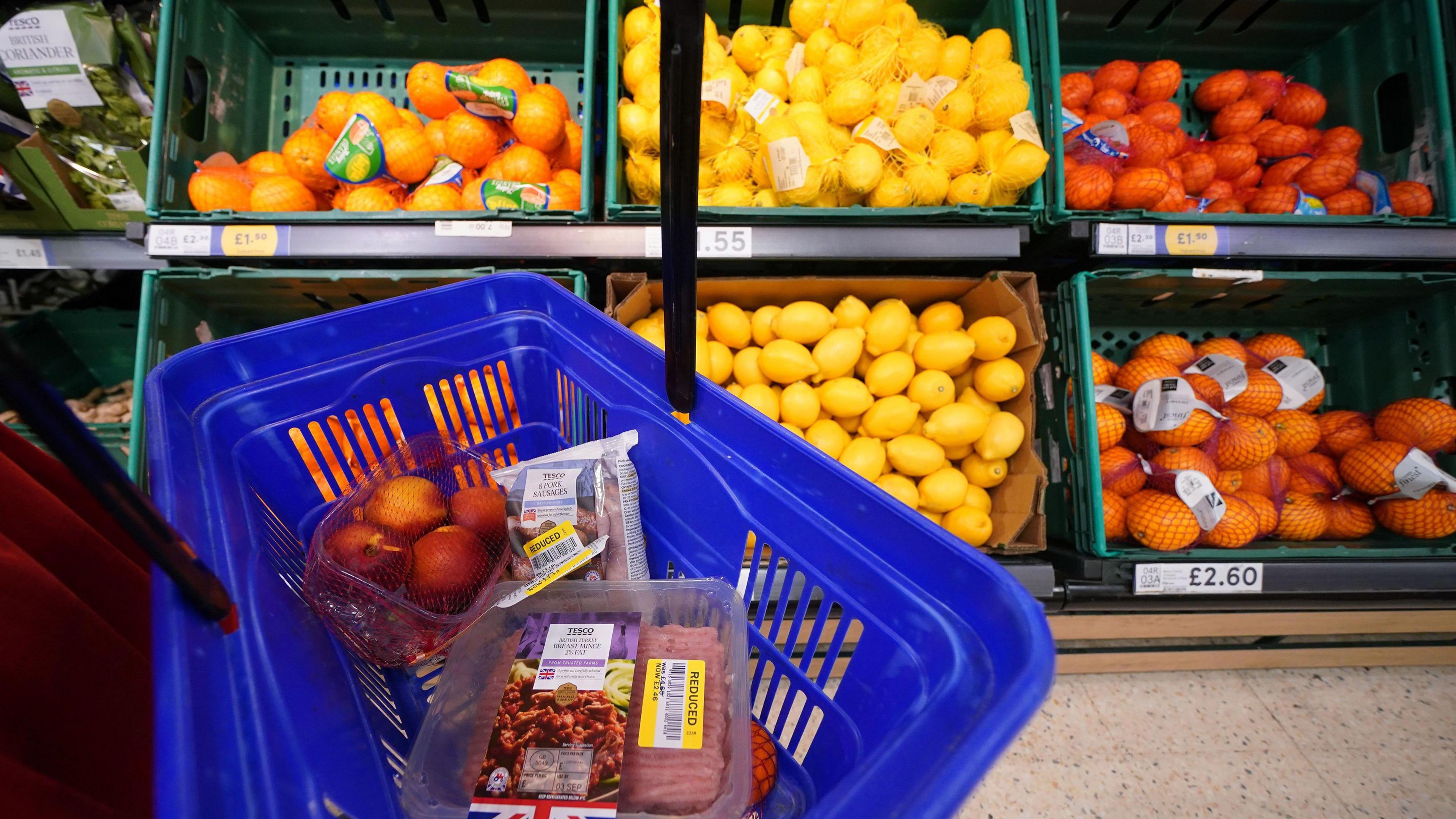 A blue basket filled with reduced priced items in front of a lemon and orange stand.