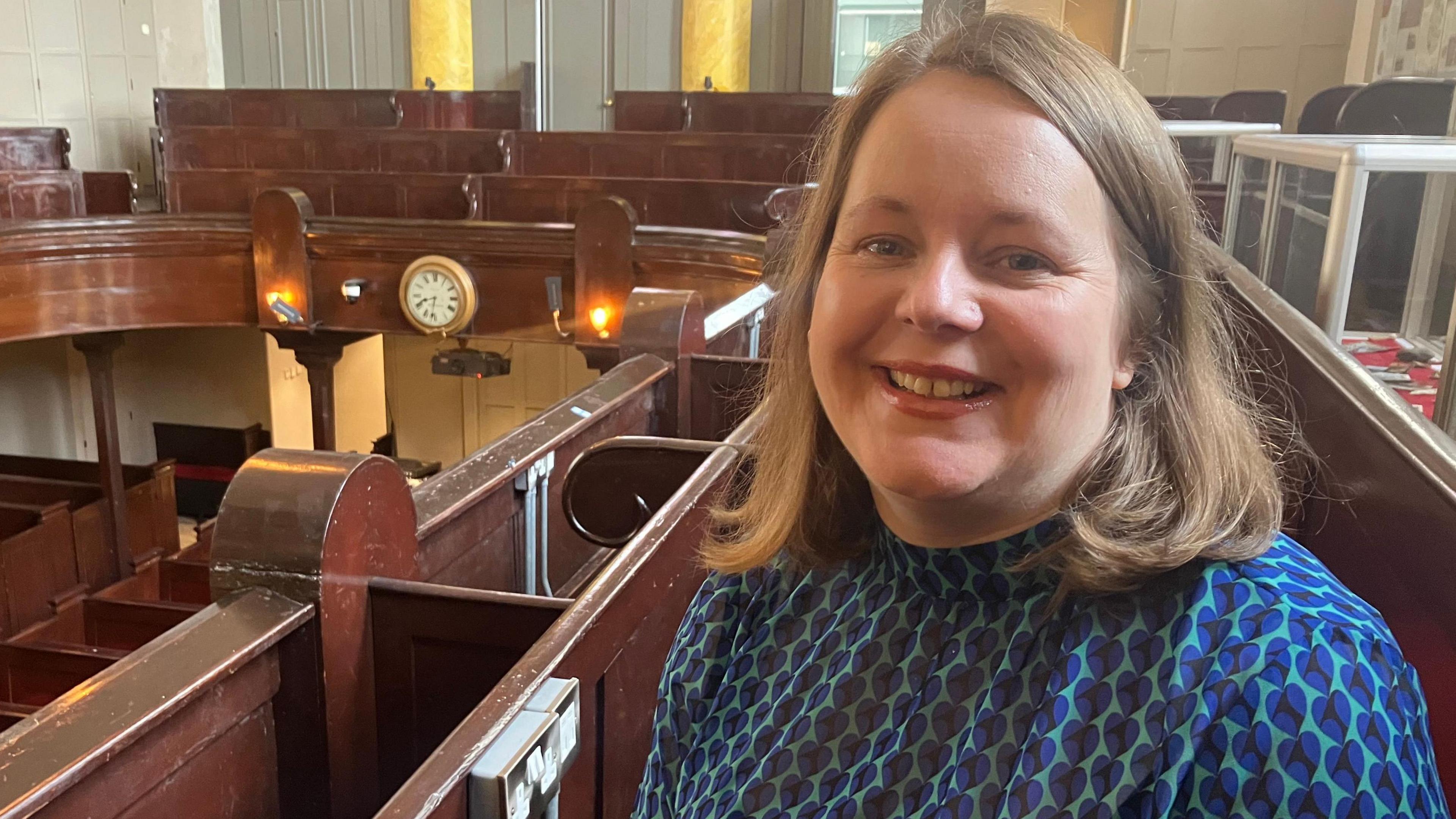 A women sits in a church pew, wearing a blue and green shirt 