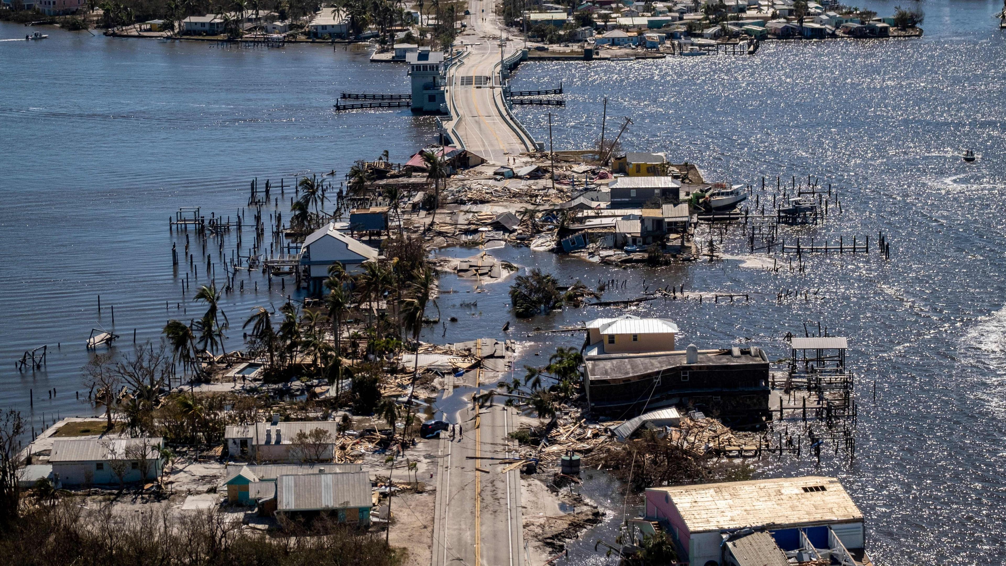 An inundated and debris-strewn coastal road in Florida with damaged houses either side