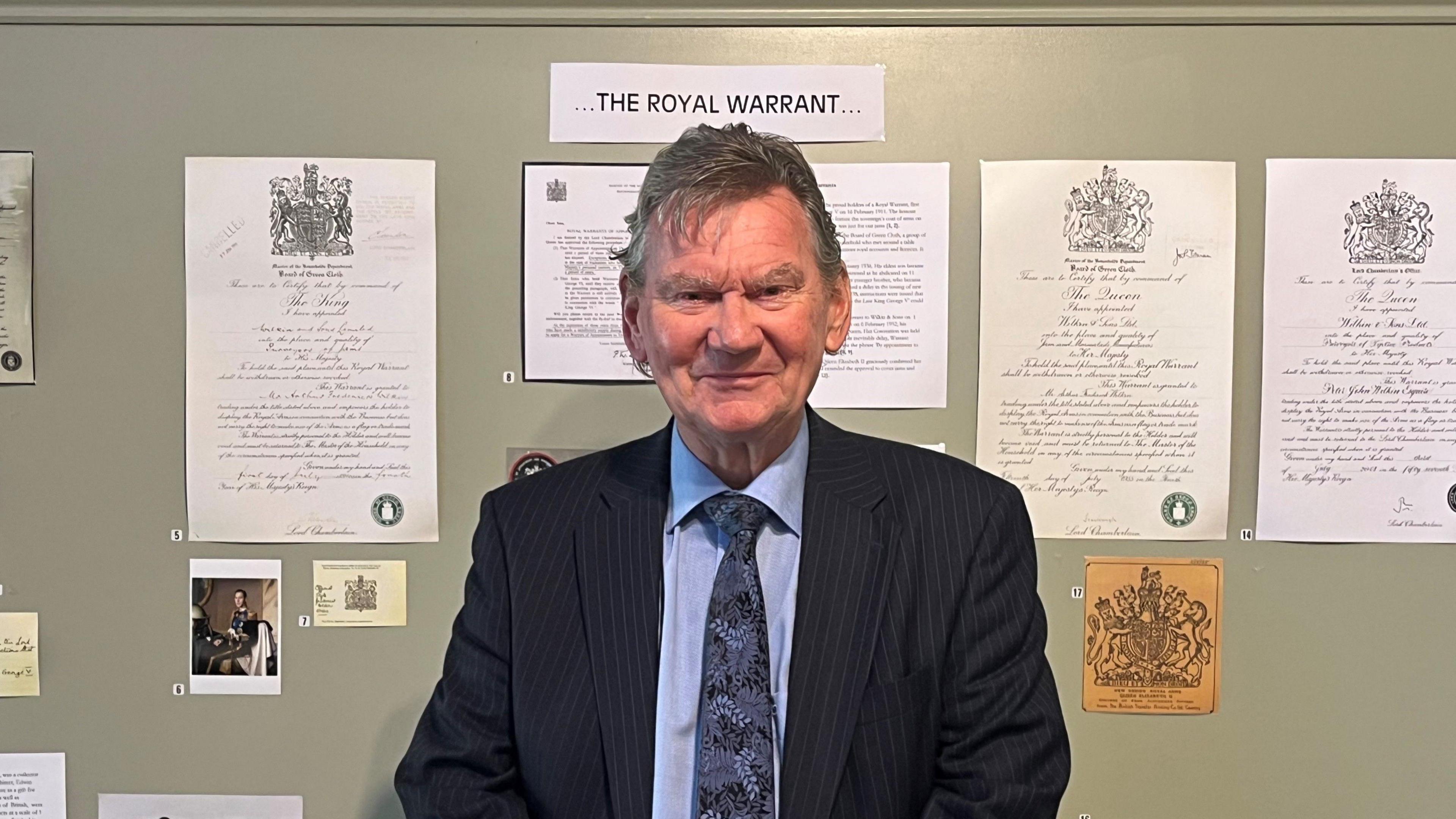 Man smiling at camera in front of a board titled 'The Royal Warrant'.