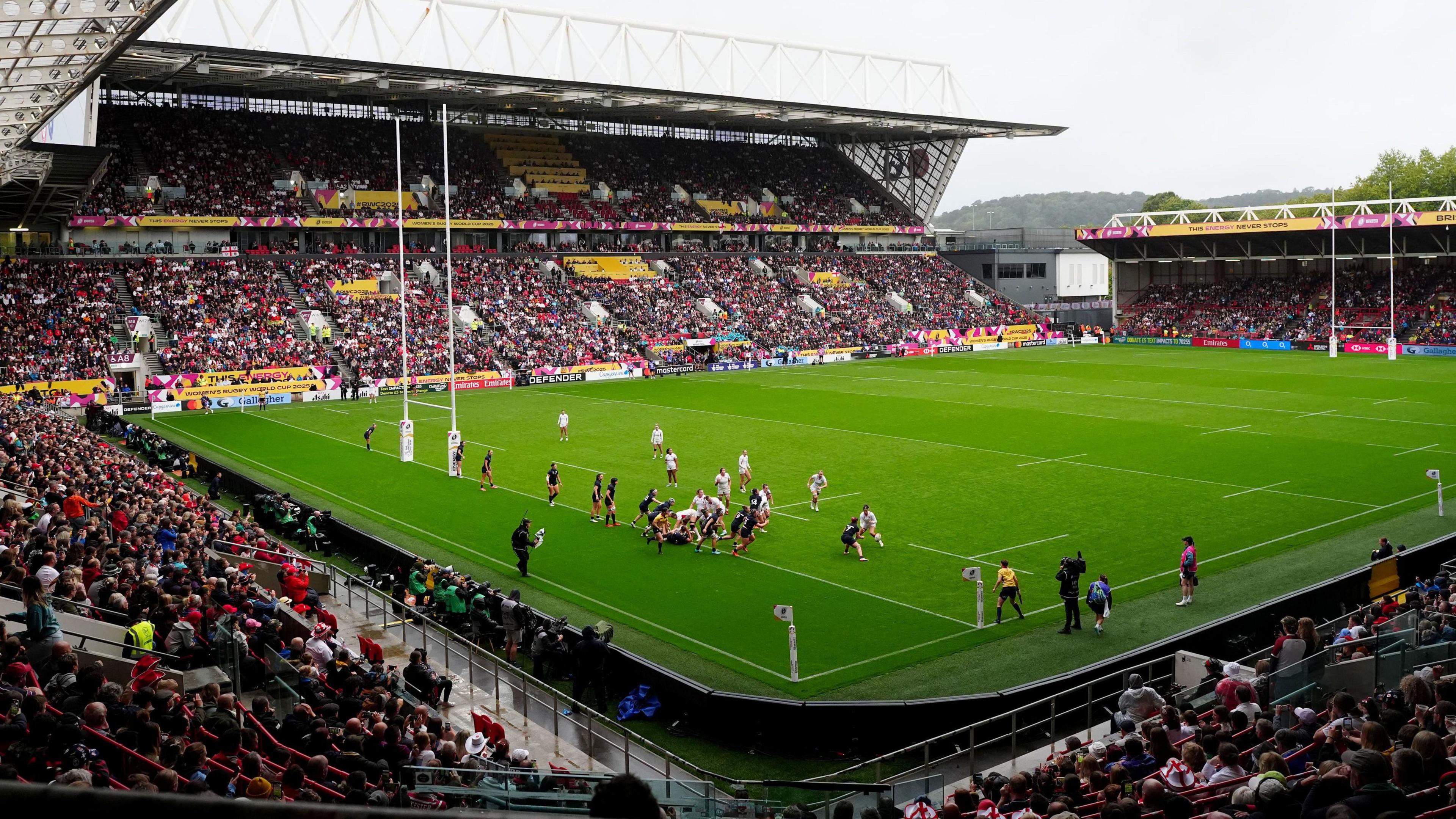 A wide shot showing the whole of the inside of Ashton Gate Stadium in Bristol during the England v Scotland women quarter final at the Women's Rugby World Cup. The stands are packed with spectators and in the match, England players are attacking very close to Scotland's try line