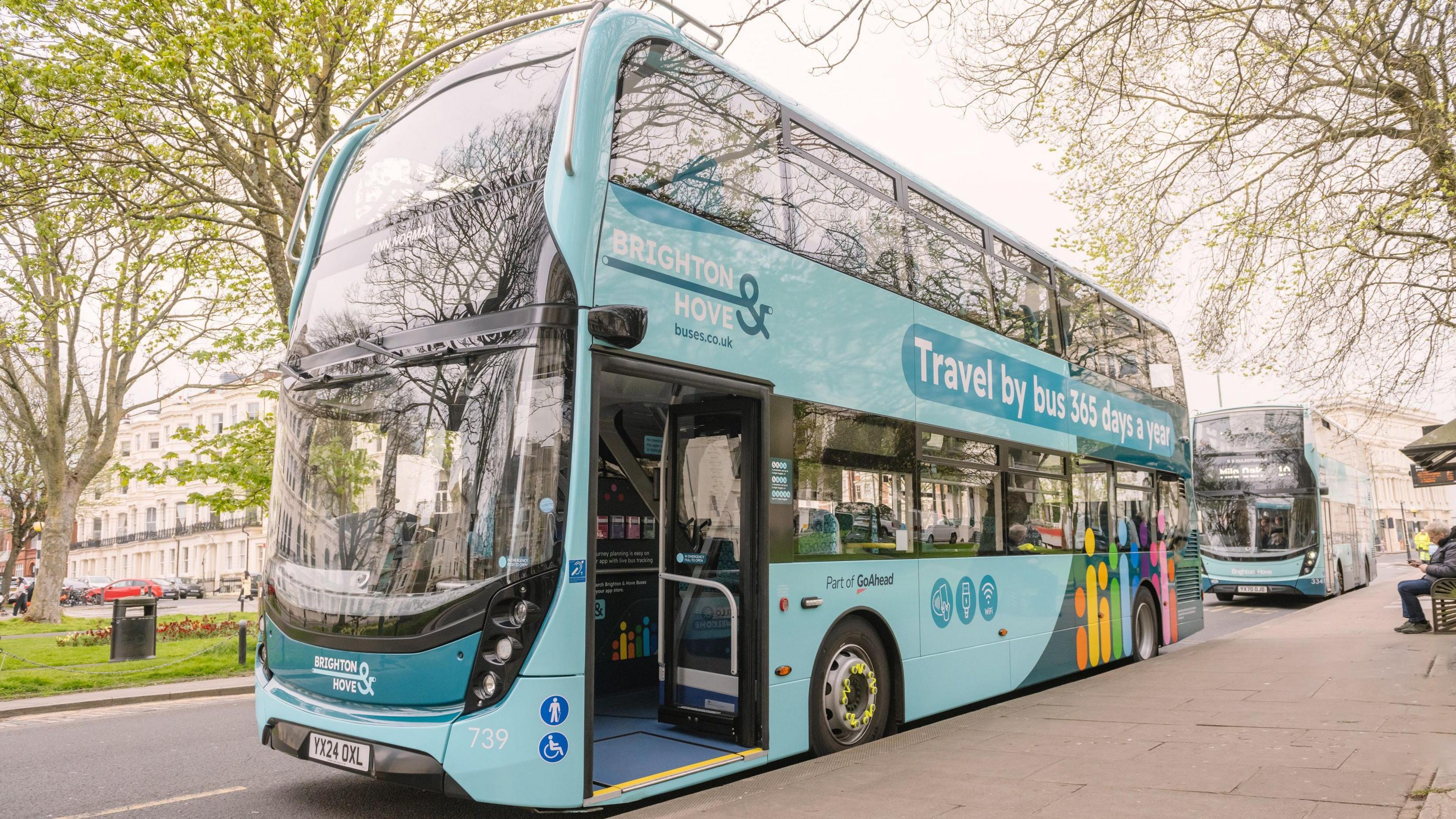 A blue Brighton and Hove bus is stationary next to the pavement with it's door open.