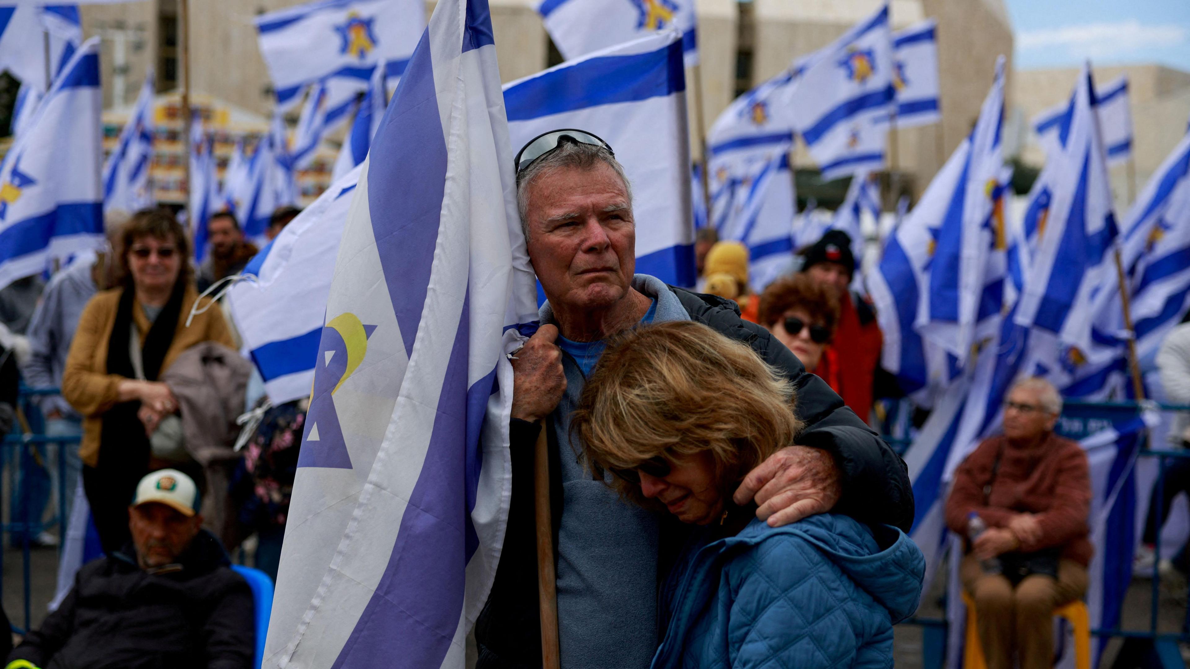 A man and woman in a crowd of Israeli flags, looking very sad. 