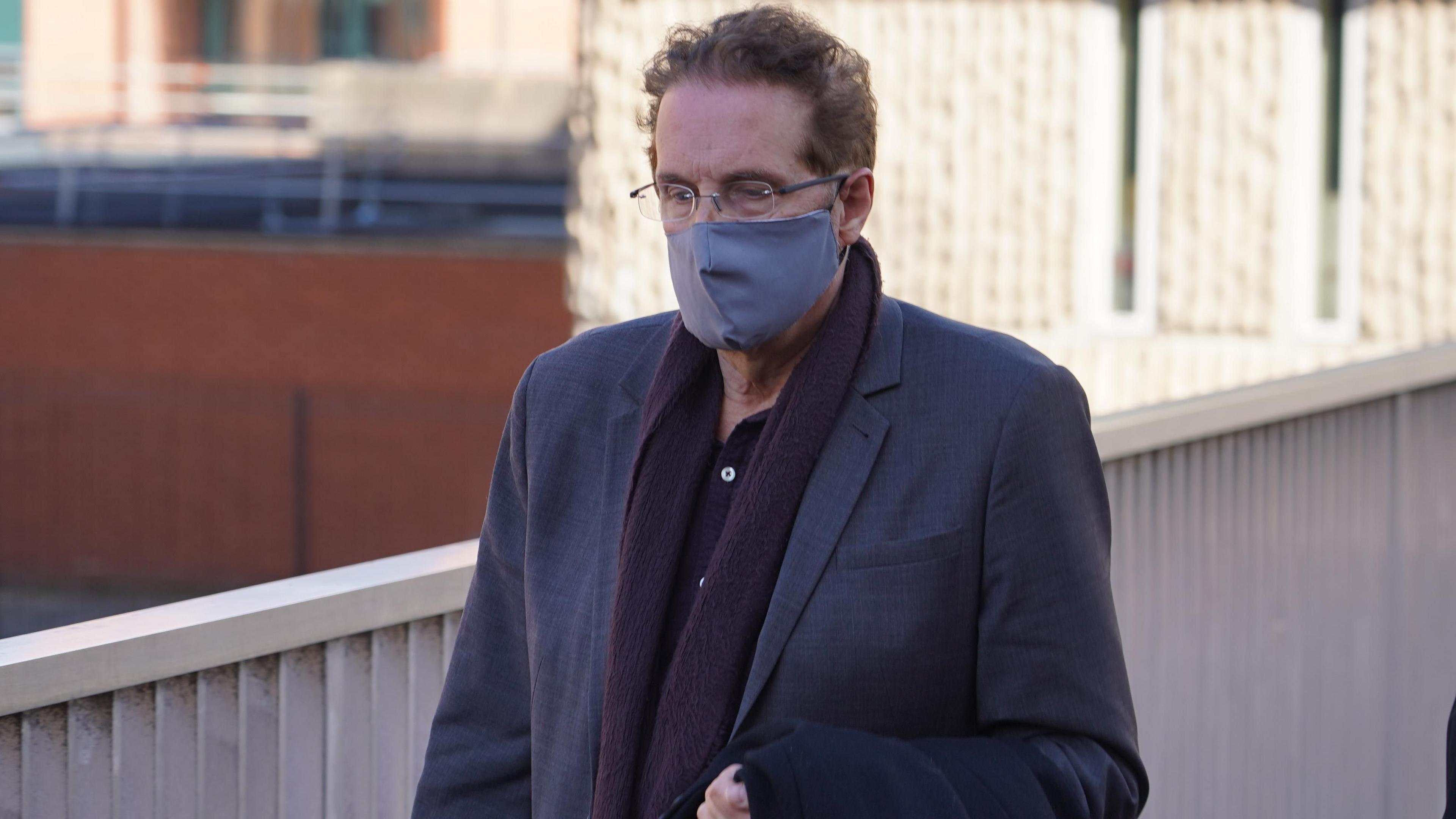 Chris Brain leaving court following an earlier appearance. He wears glasses and a face covering, as well as a dark-coloured blazer and scarf.