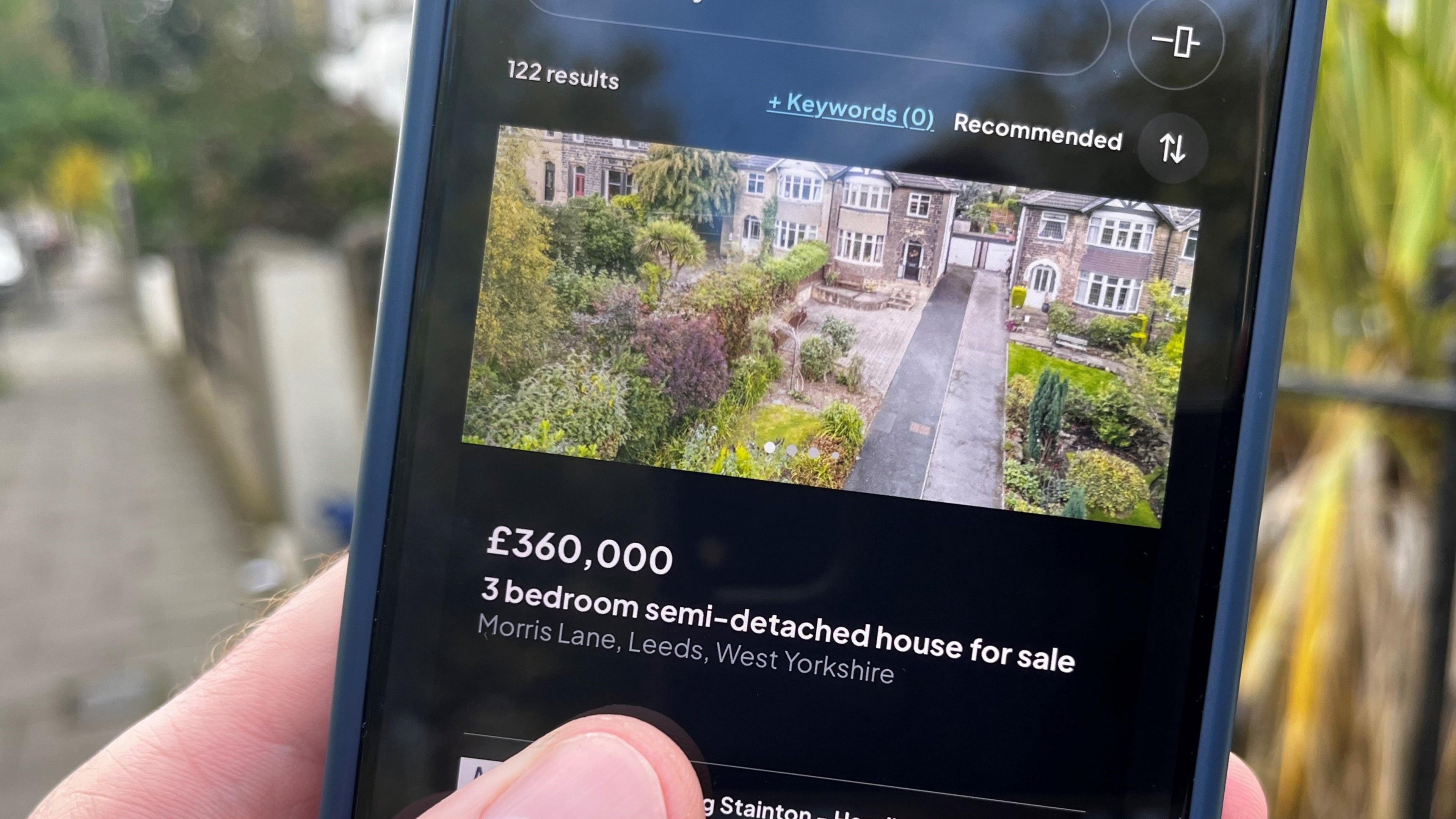 Someone holding a phone showing a property portal site advertising a £360,000 three bedroom semi-detached house for sale