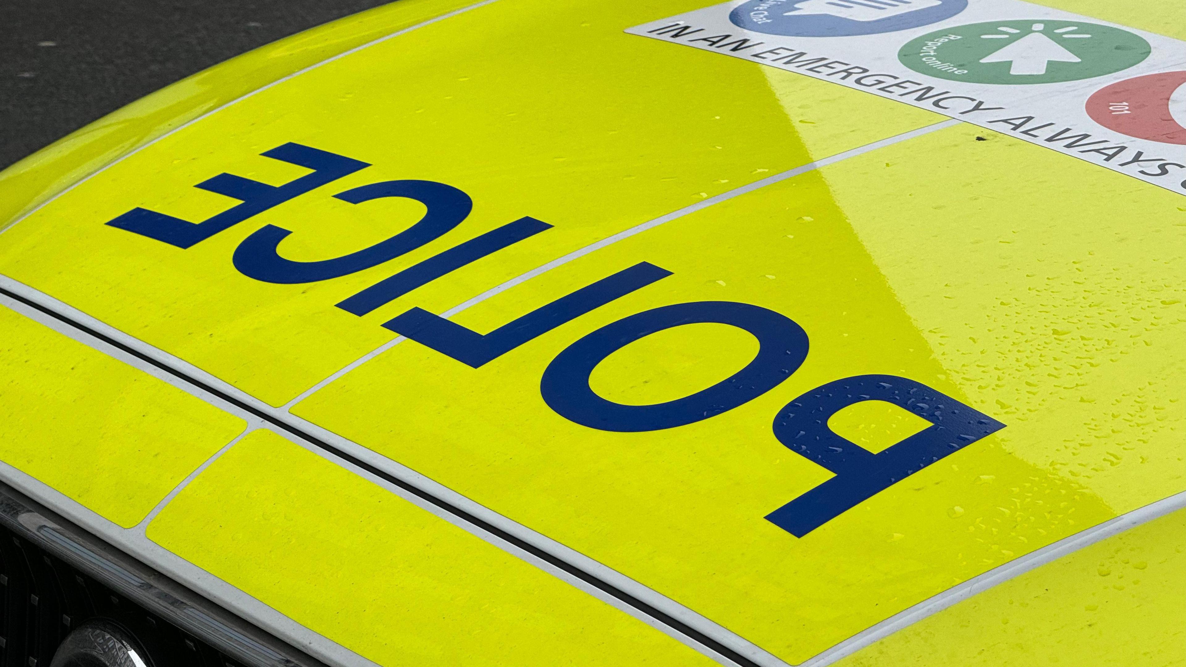 The yellow high visibility bonnet of a police car, with the word police in reverse letters in dark blue.