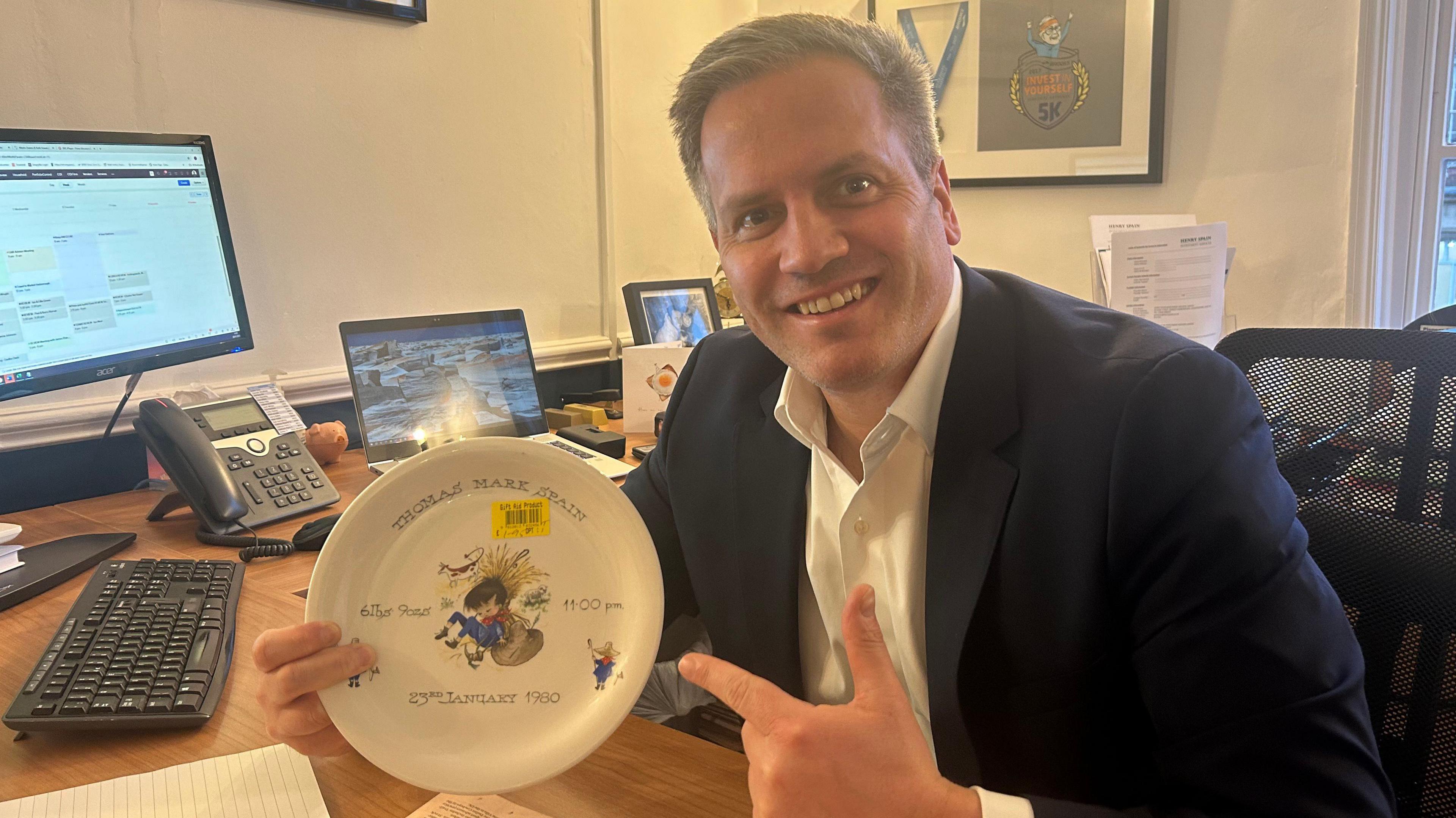 Tom Spain is sitting at a desk pointing at the plate that has been returned to him 