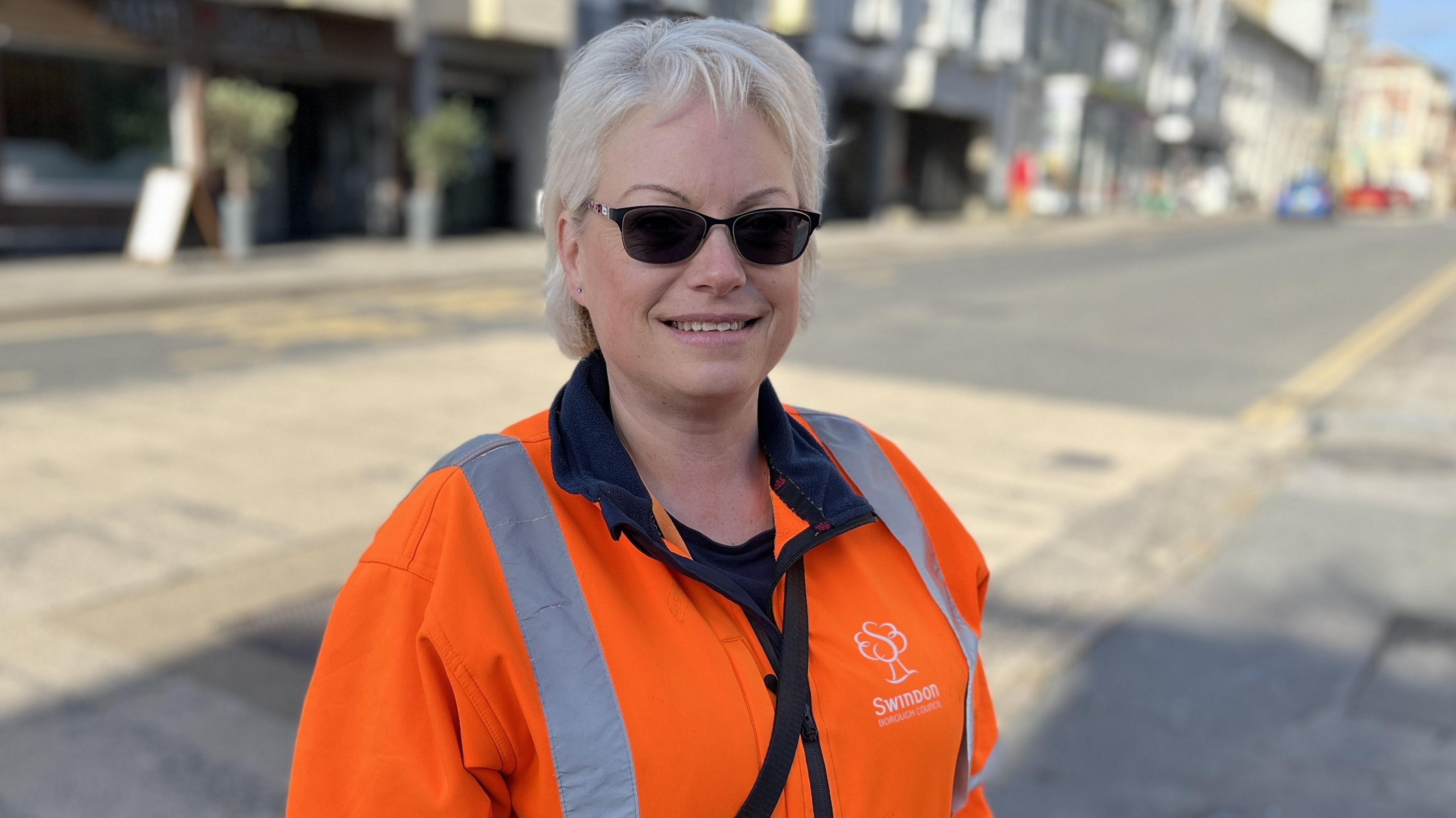 Highways Inspector, Marcia Belcher, with short blonde hair wearing sunglasses and an orange SBC high visibility jacket