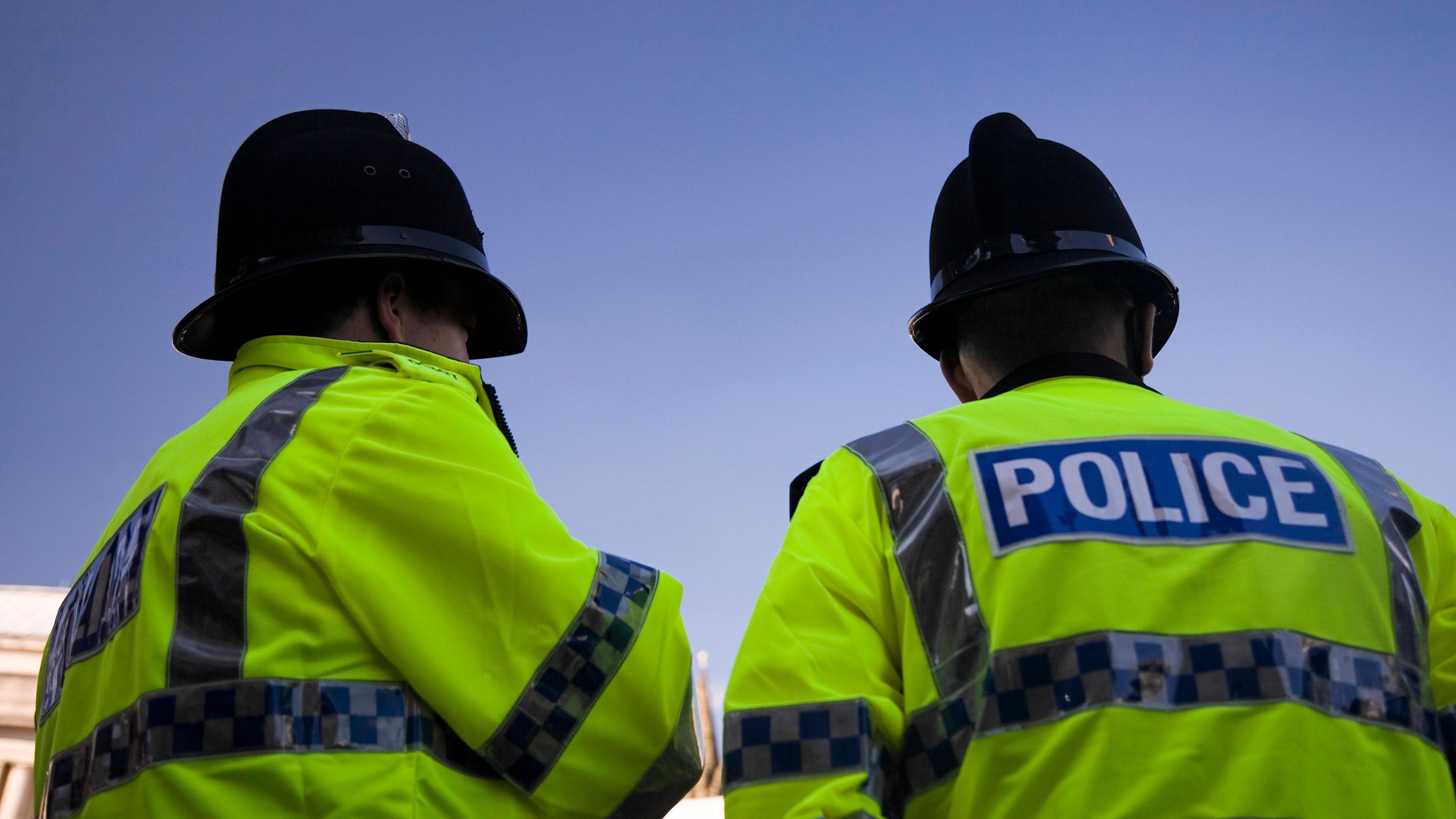 Two police officers in uniform with their backs to the camera