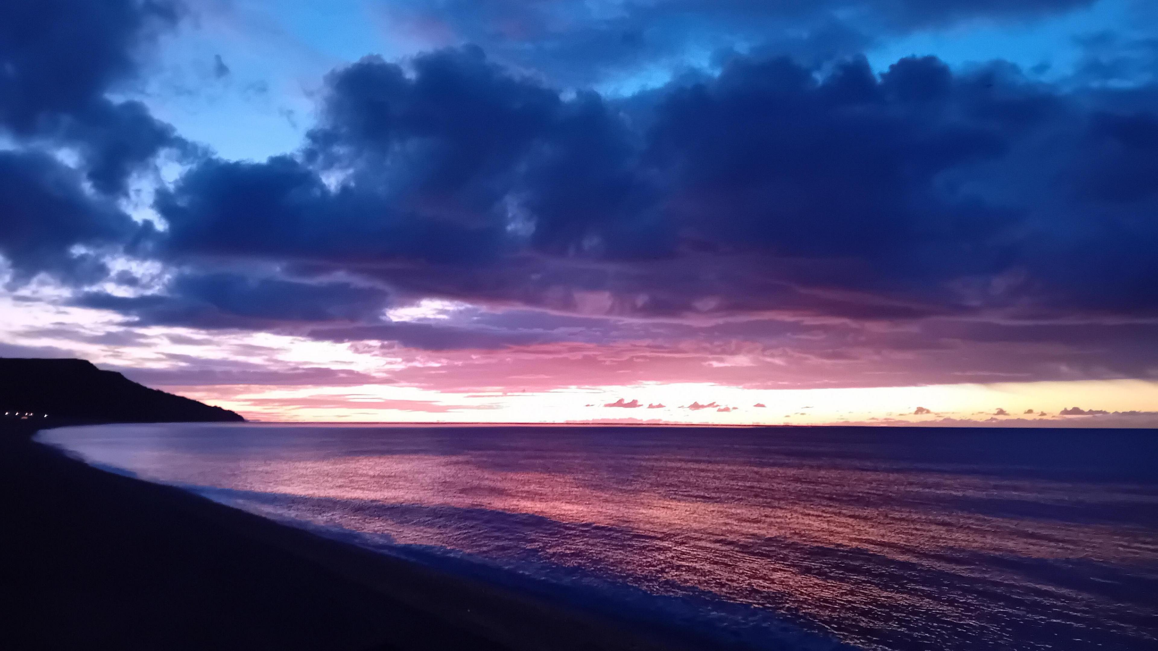 A beach scene in Seaton, Devon is cast in a purple glow, with the sea and sky framing an area of yellow amid the sunrise 