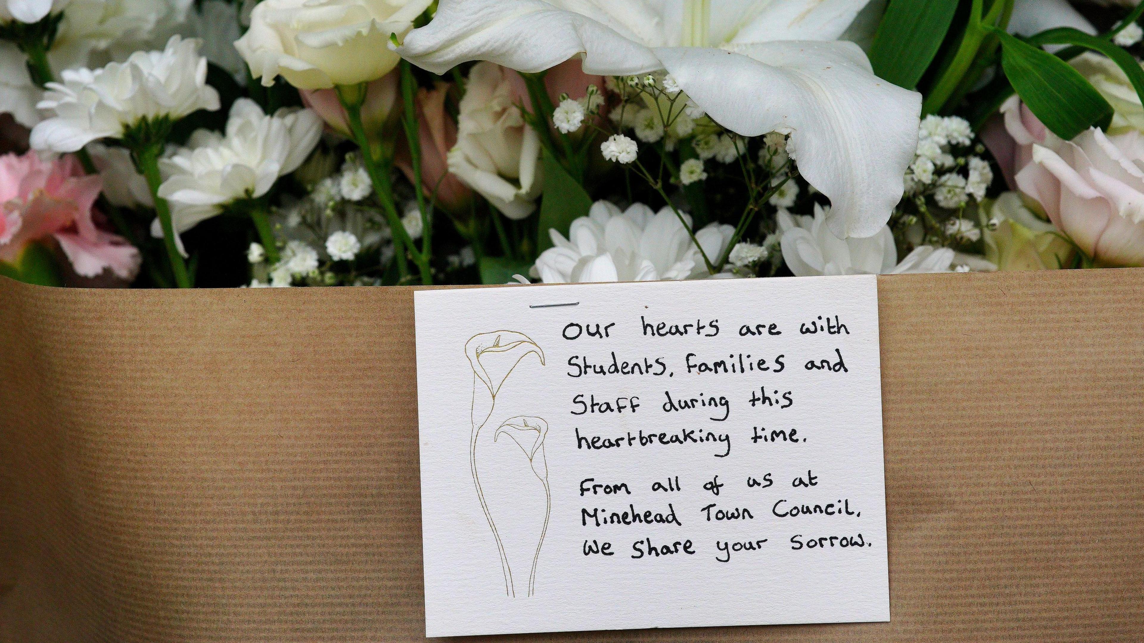 A card on a bouquet of flowers reads: Our hearts are with students, families and staff during this hearbreaking time. From all of us at Minehead Town Council, we share your sorrow.