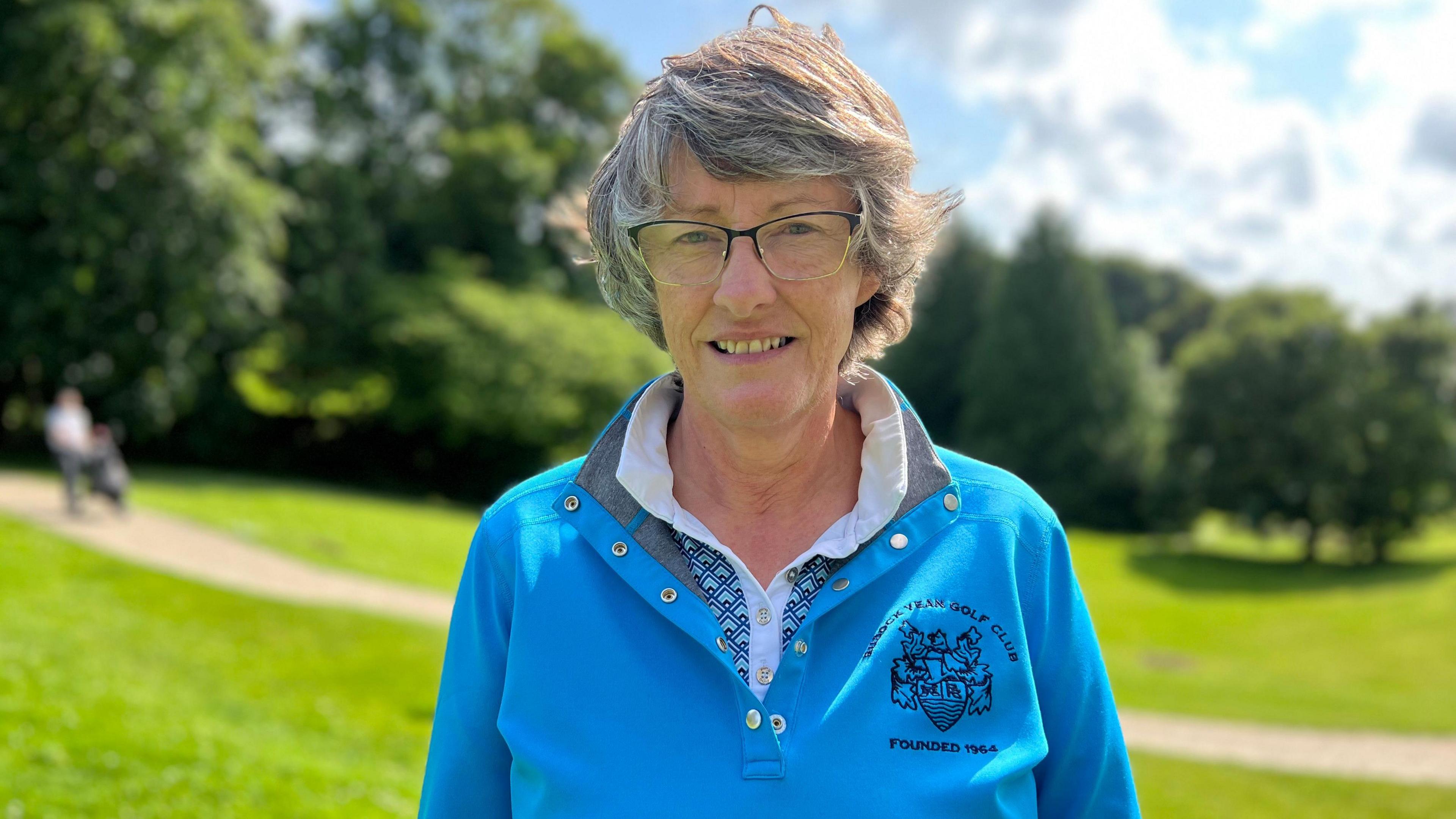 A woman wearing a bright blue golfing fleece smiles for the camera 