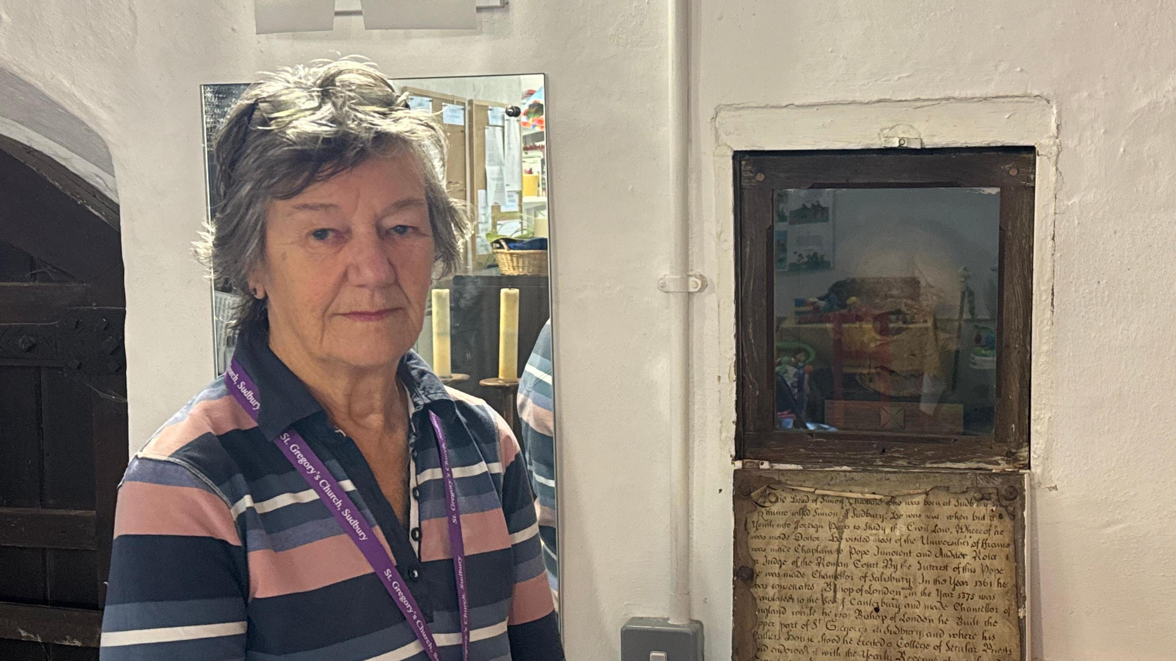 Mandy Turner, who is wearing a striped top and looking directly into the camera, standing next to the cubbyhole in which the skull sits.