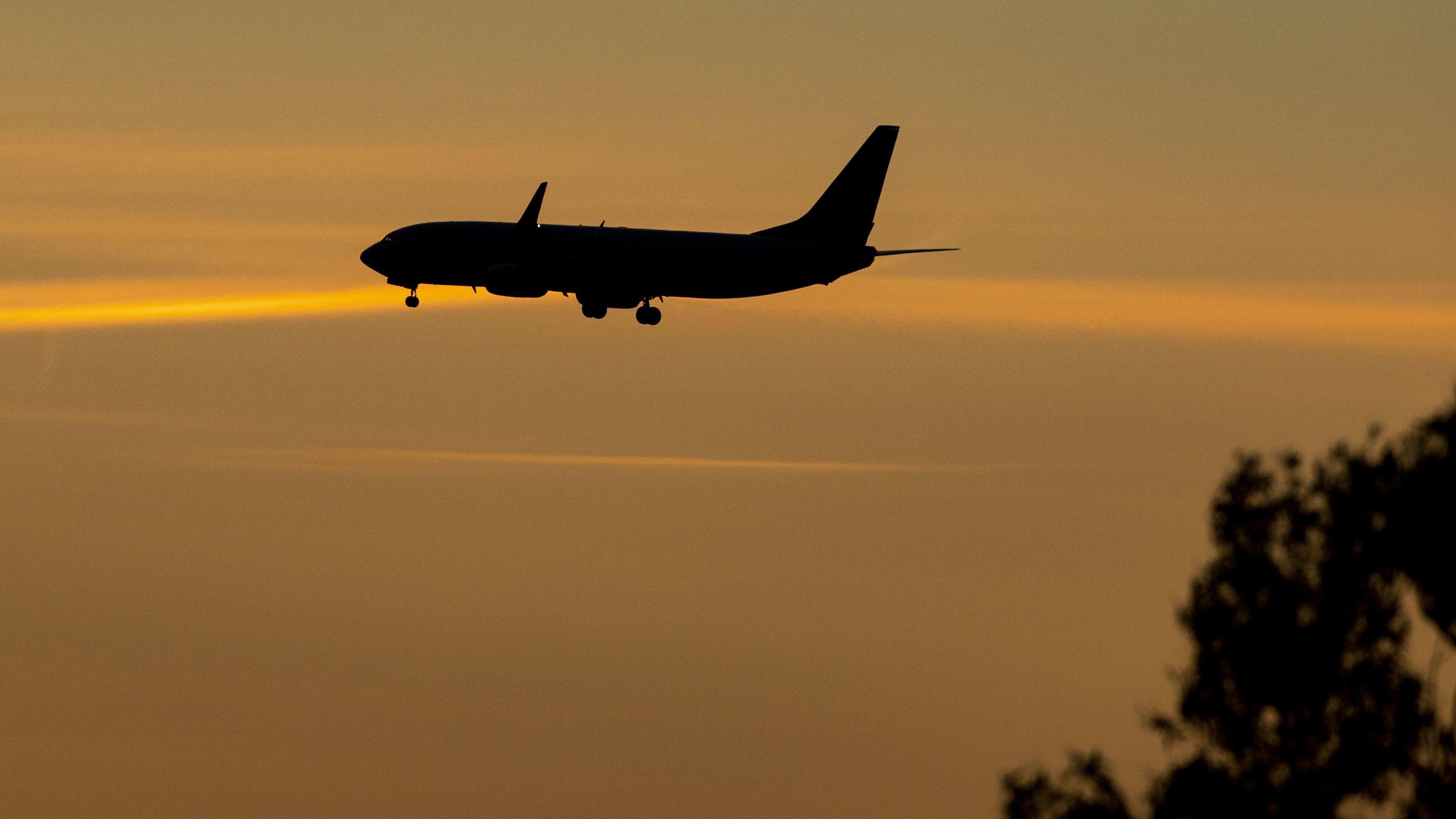 Silhouette of a plane flying through the sky at sunset. 