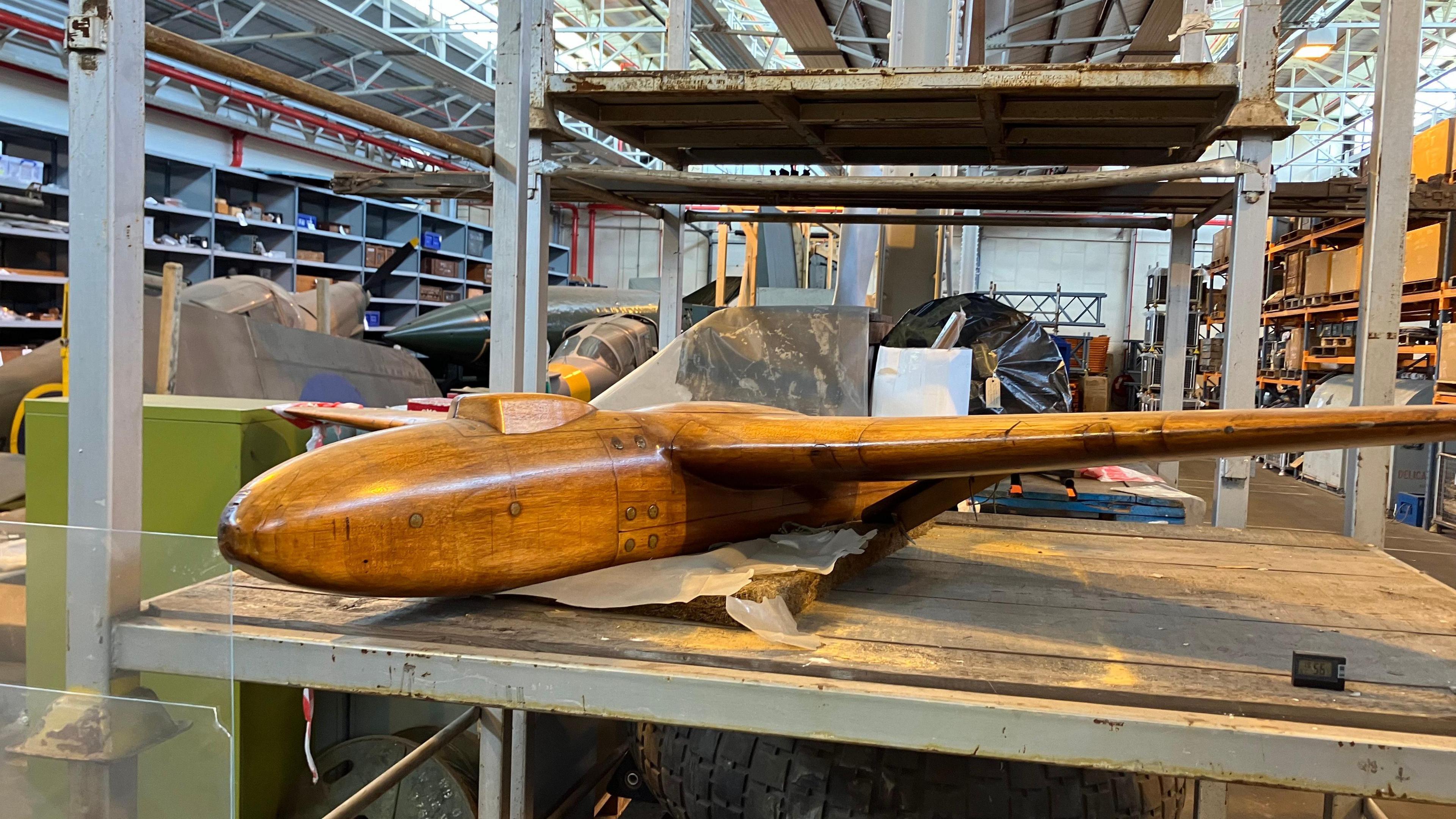 A wooden model of a plane sitting on a shelf in the middle of a large warehouse. 