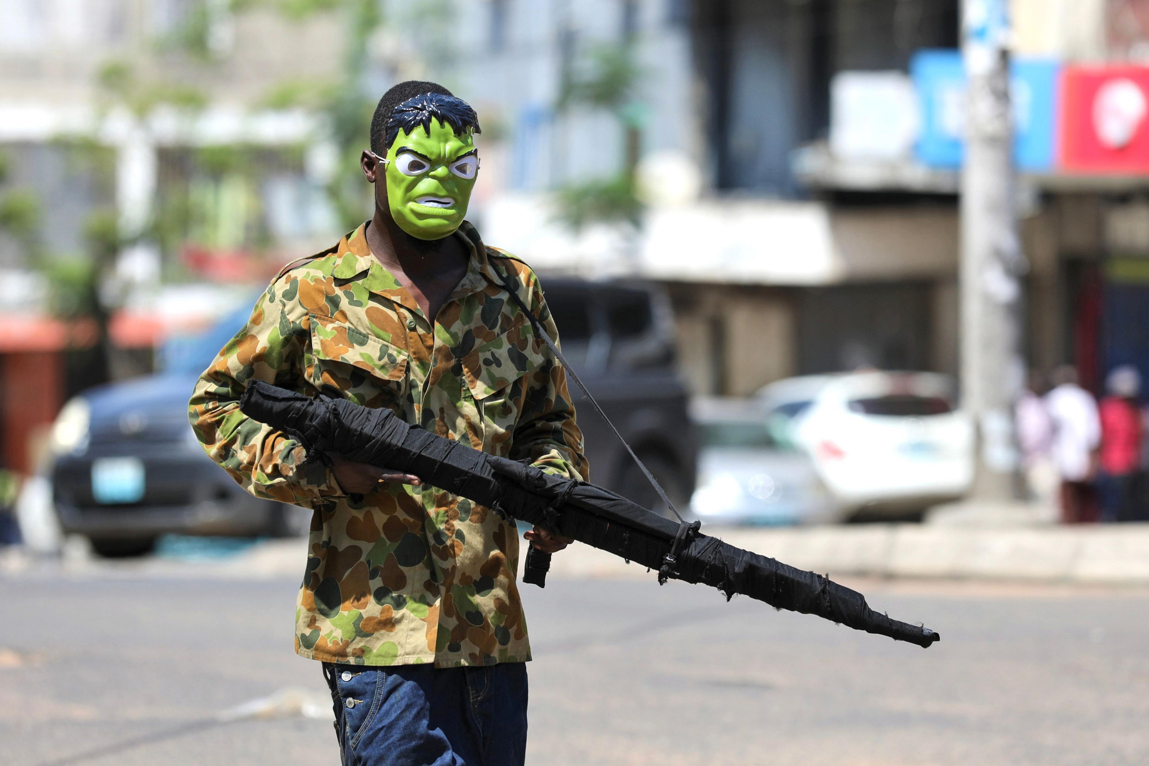 A man walks down the street with a Hulk mask and a dummy rifle.