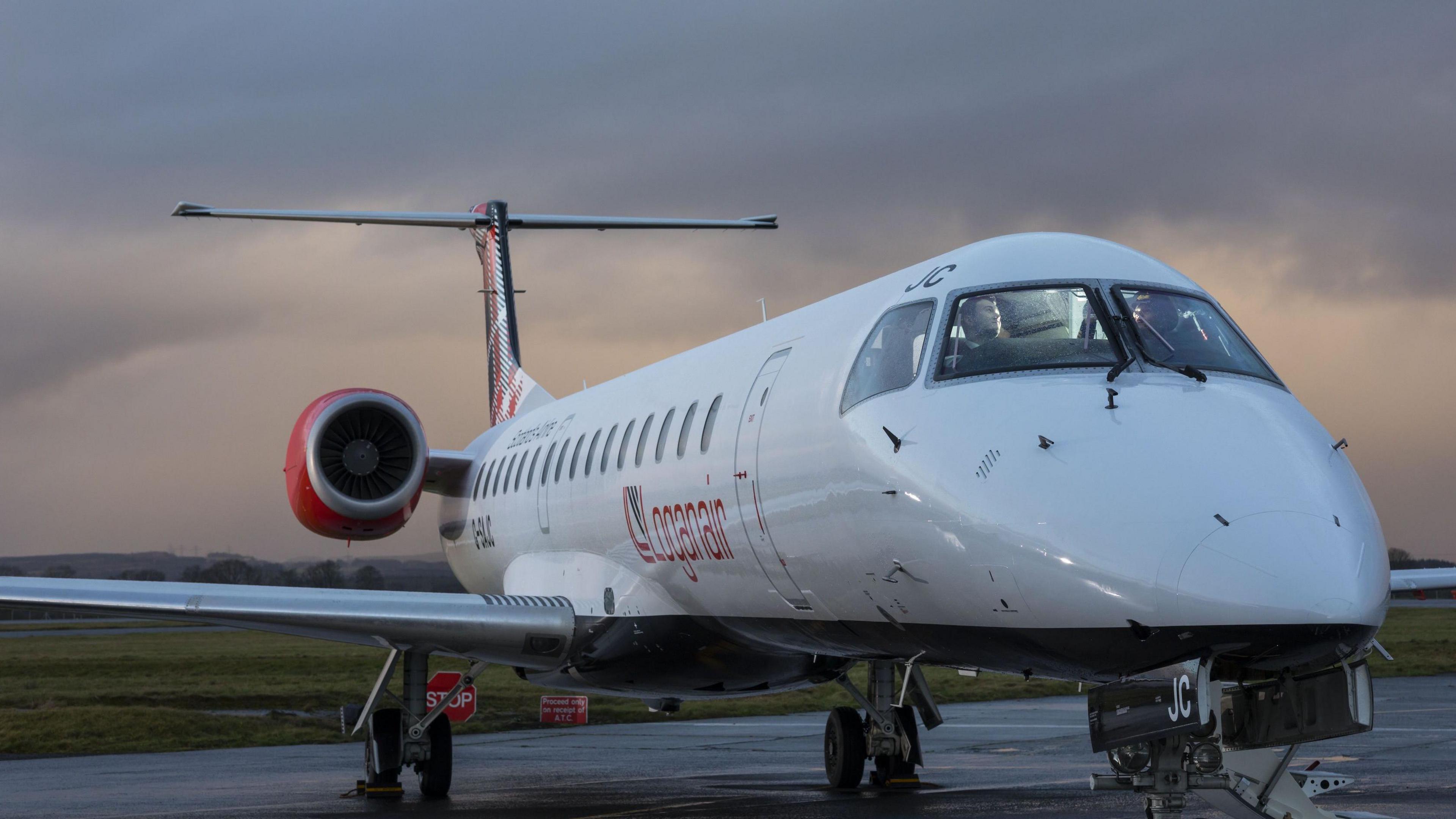 The nose of a Loganair plane. It is white and has red features and is stationary at an airport.