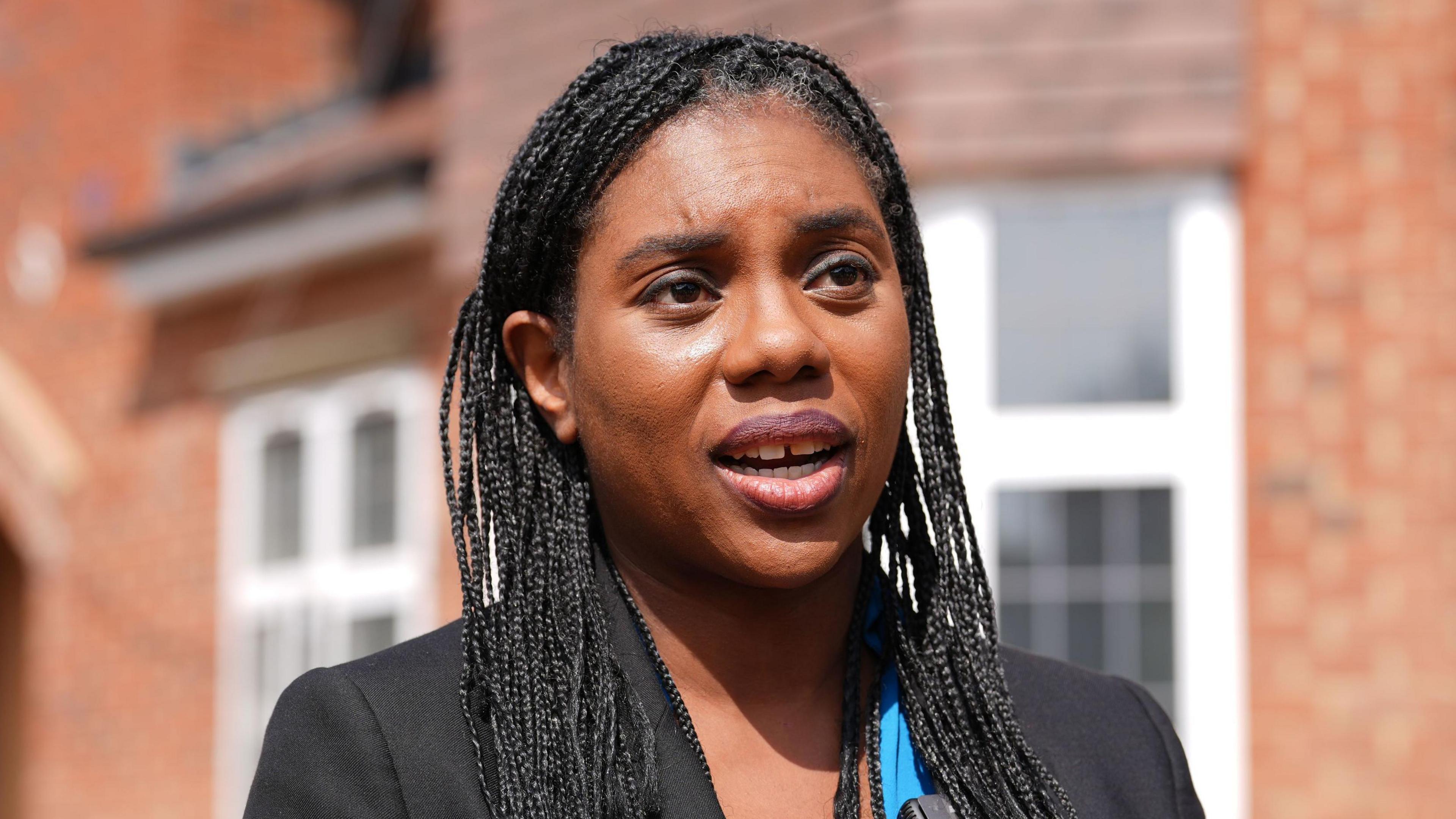 Leader of the Conservative Party Kemi Badenoch stands outside a housing estate on a sunny day