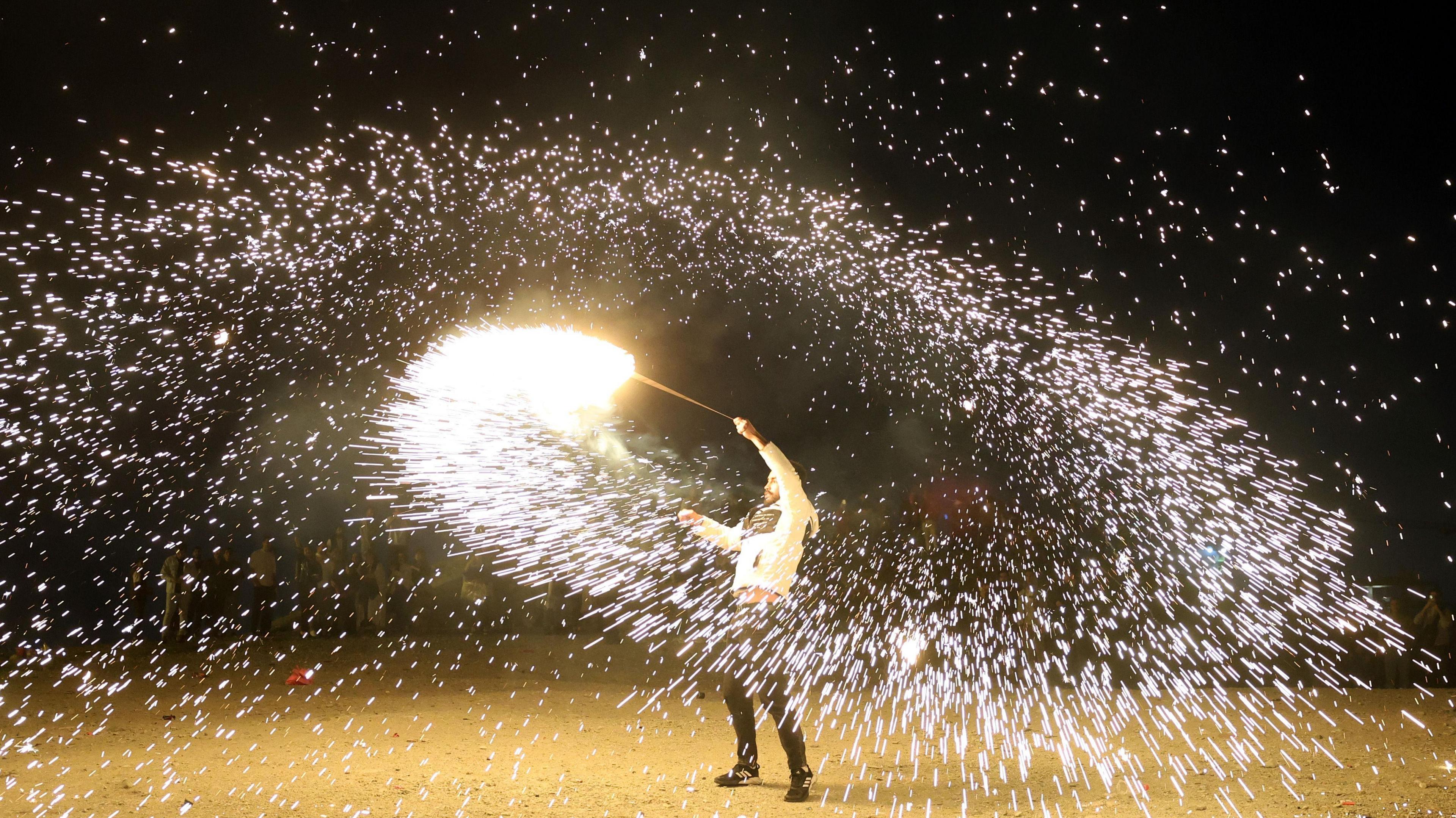 A man spins a fire stick around above his head, spraying sparks out around him