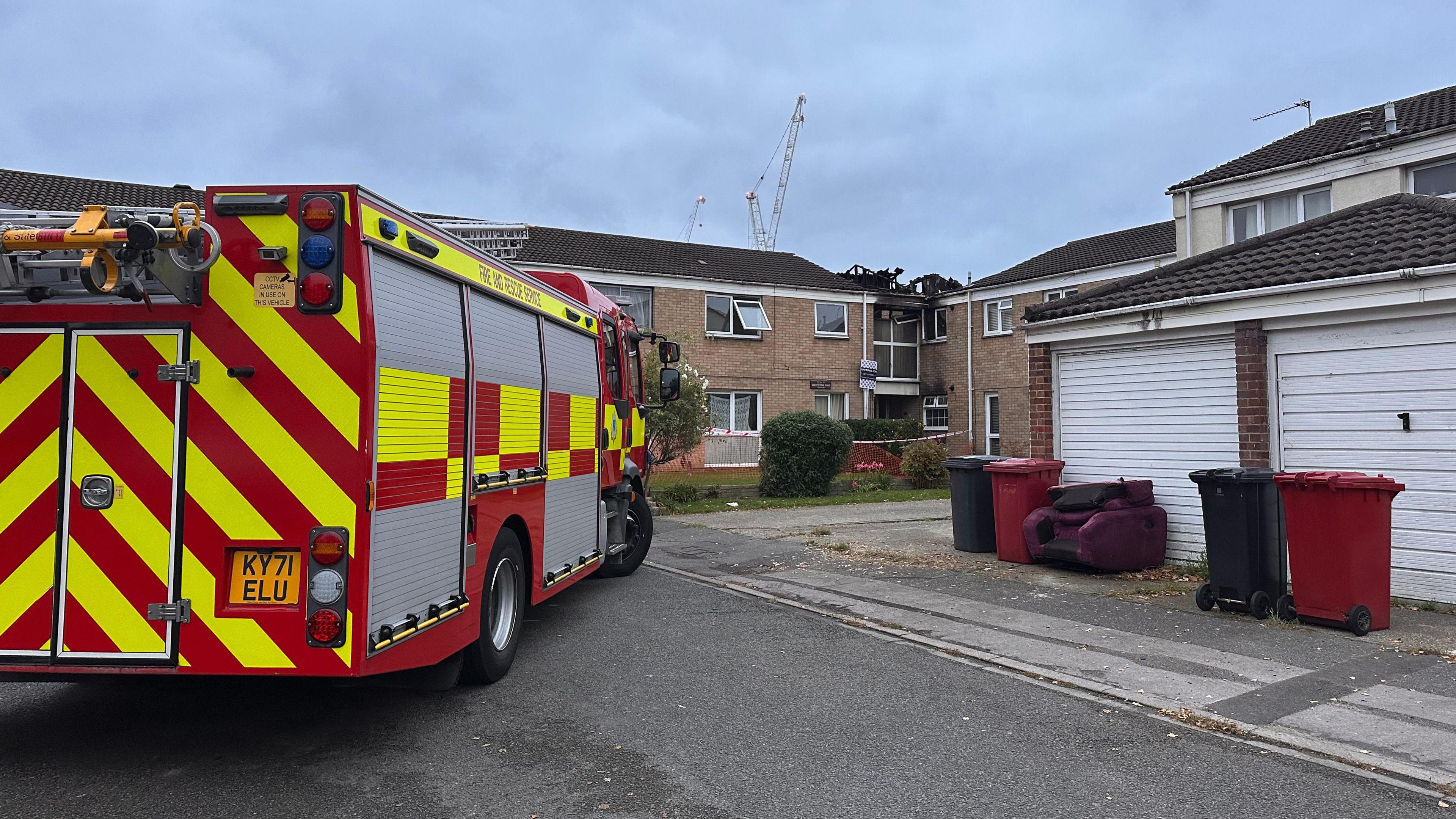 Fire engine parked up by garages and a series of low-rise flats.
