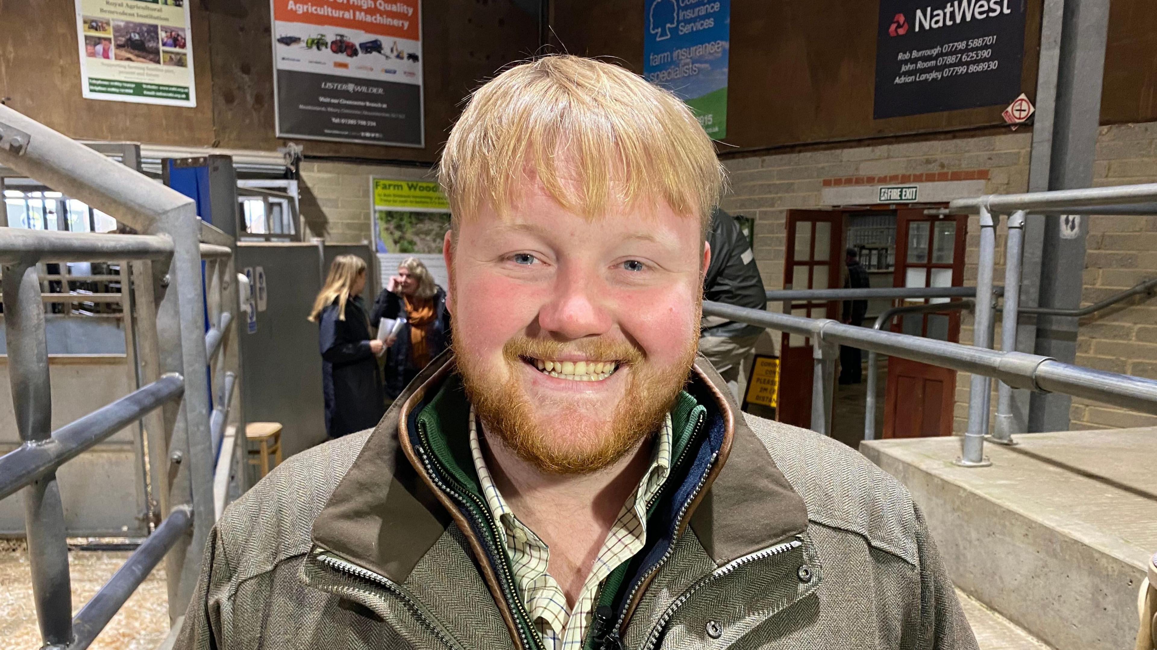 Kaleb Cooper pictured wearing a tweed jacket and checked shirt. He has a ginger beard and short ginger hair.