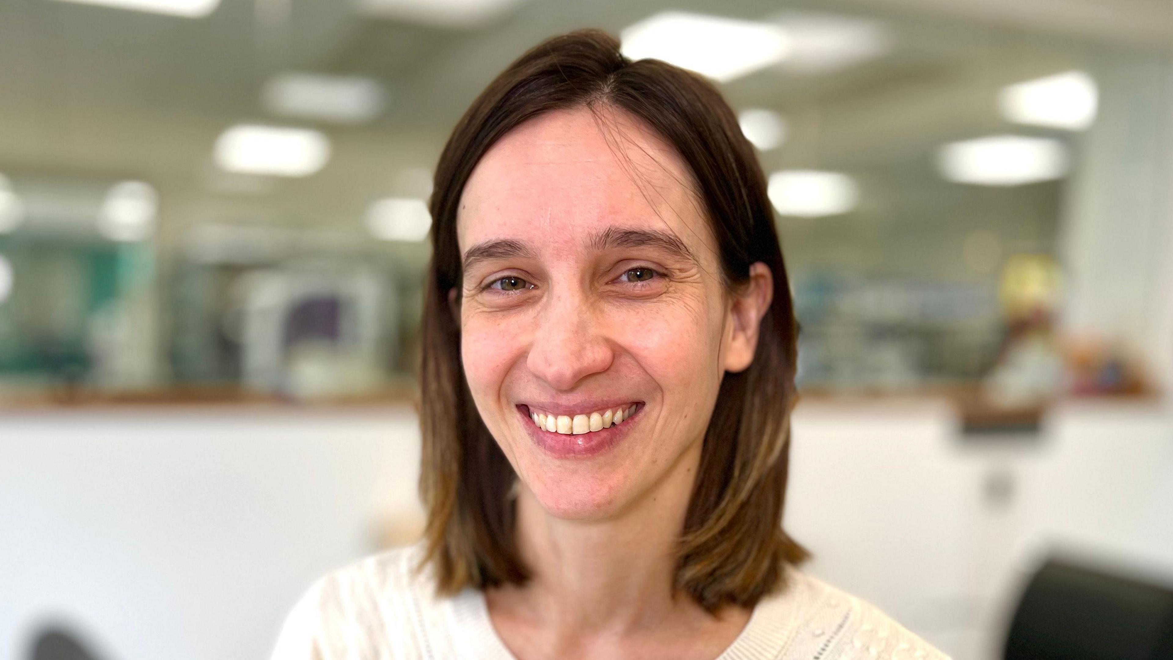 Dr Carolina Grandellis, who has shoulder-length brown hair, wearing a white button-up top in a laboratory.