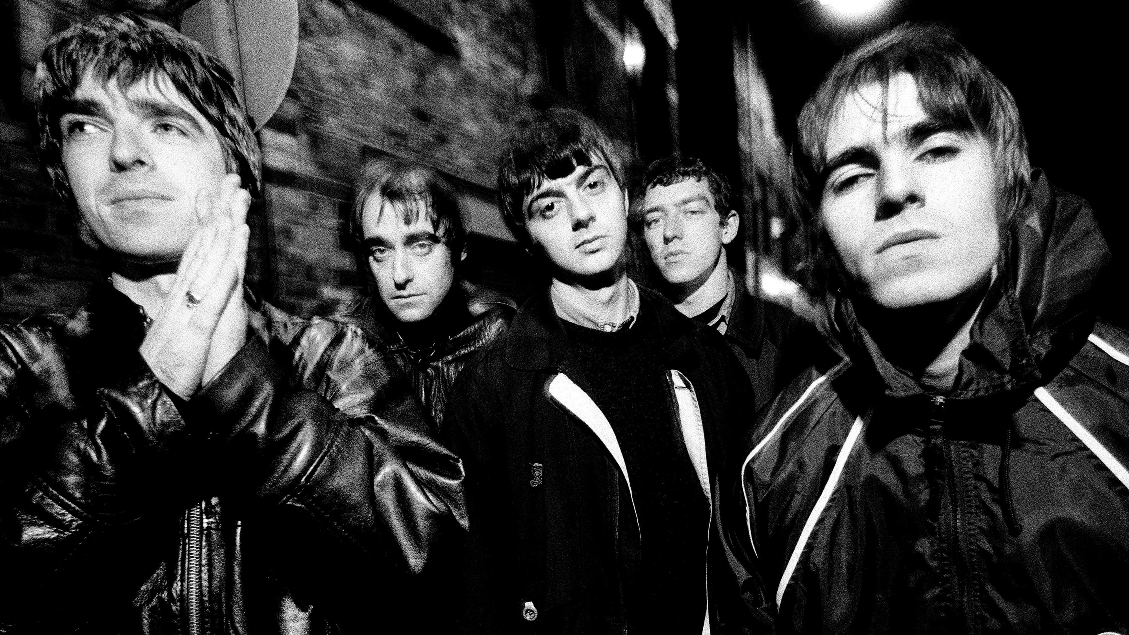 A black-and-white photo of the original Oasis line-up in 1993. Left to right: Noel Gallagher, Paul Arthurs (aka Bonehead), Paul McGuigan, Tony McCarroll,Liam Gallagher