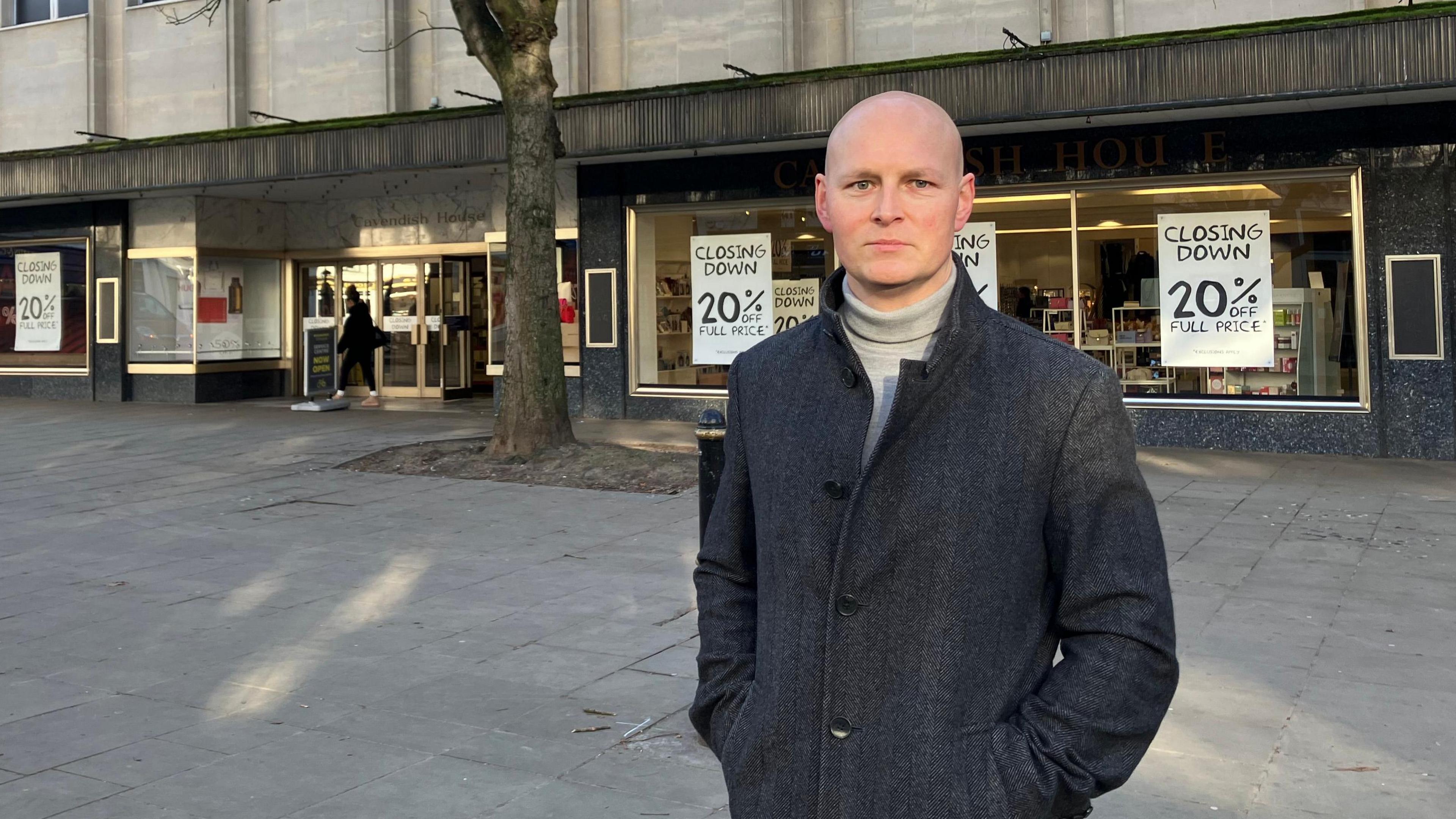 Max Wilkinson in front of a shop. He is wearing a grey coat.